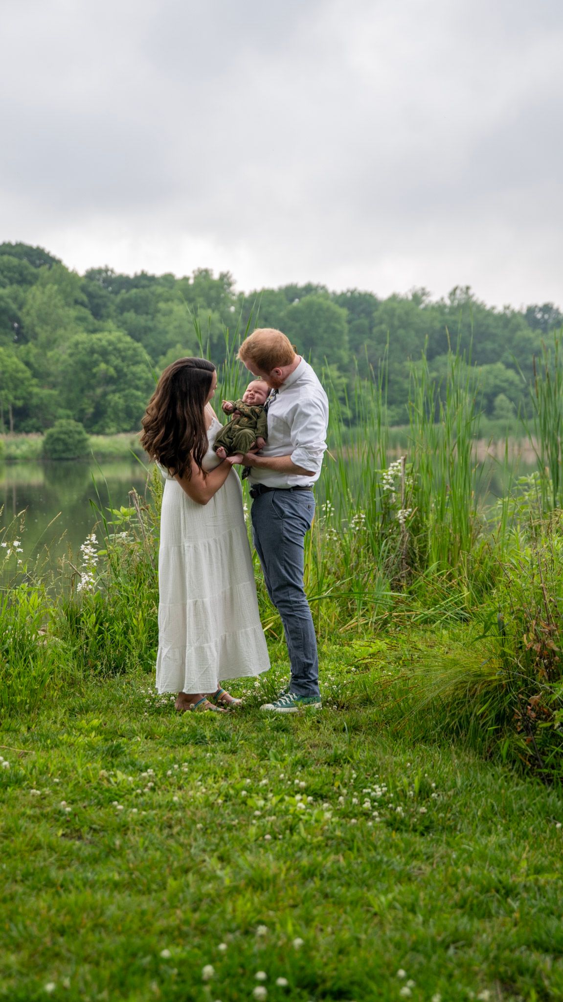 A family shares a tender moment together in a meadow by a lake.