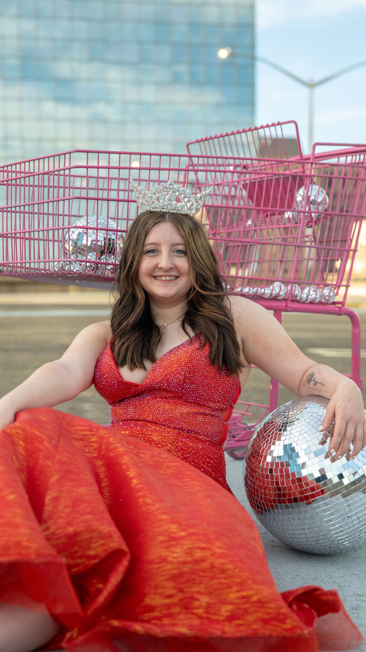Artistic fashion photos with a red dress, disco balls, and pink shopping carts against a glass building.