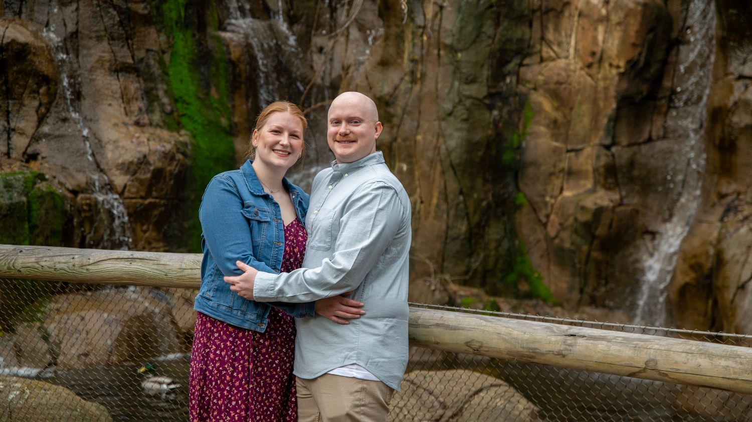 A couple poses together against a dramatic rock wall backdrop with a waterfall.