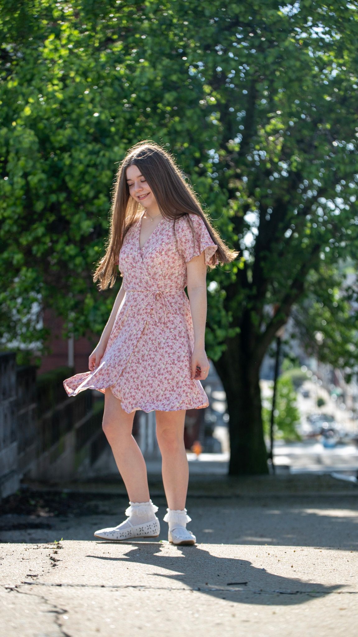 Playful outdoor poses in a floral dress under tree canopy.