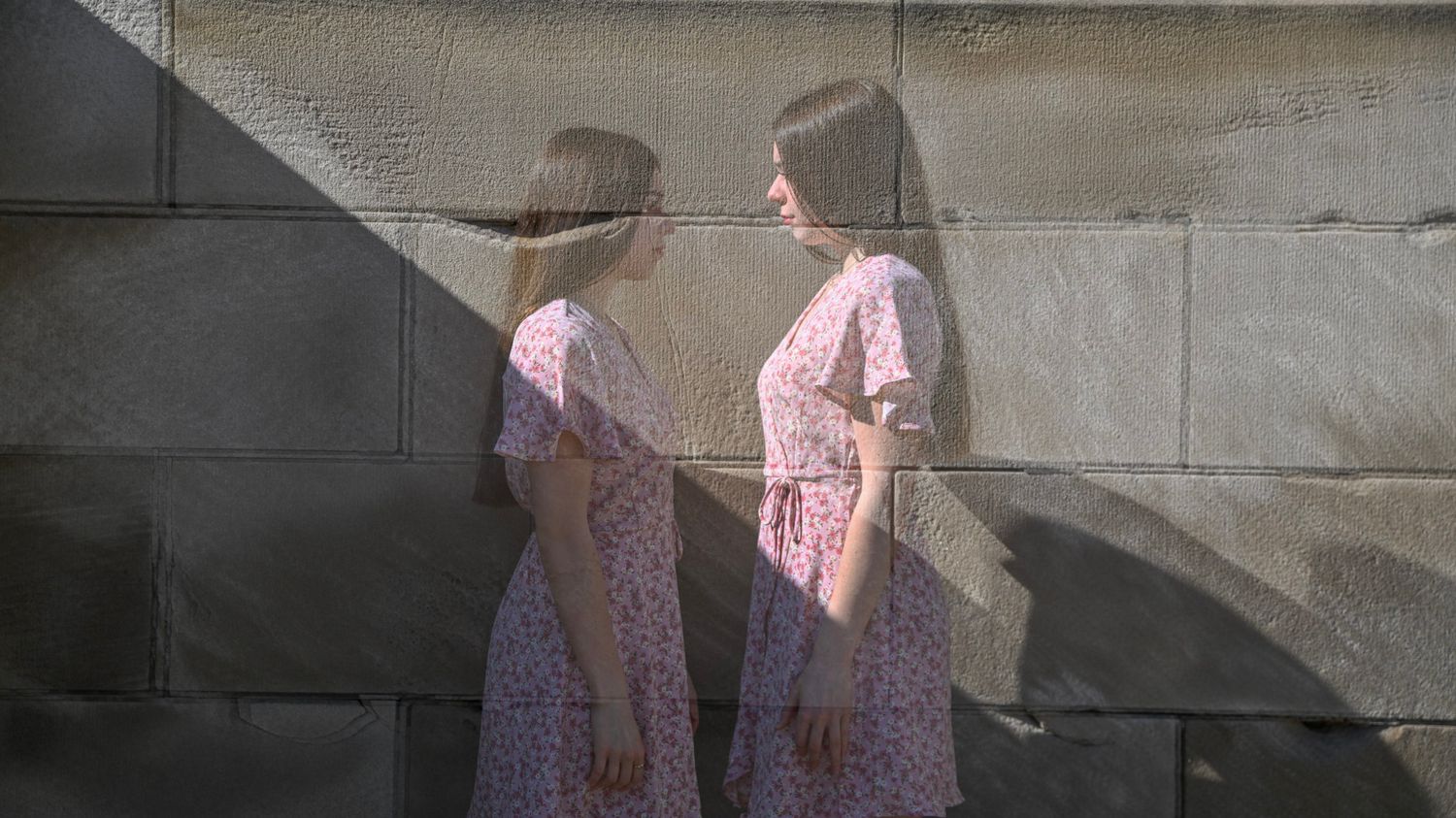 Silhouettes against a concrete wall wearing a pink floral dress.