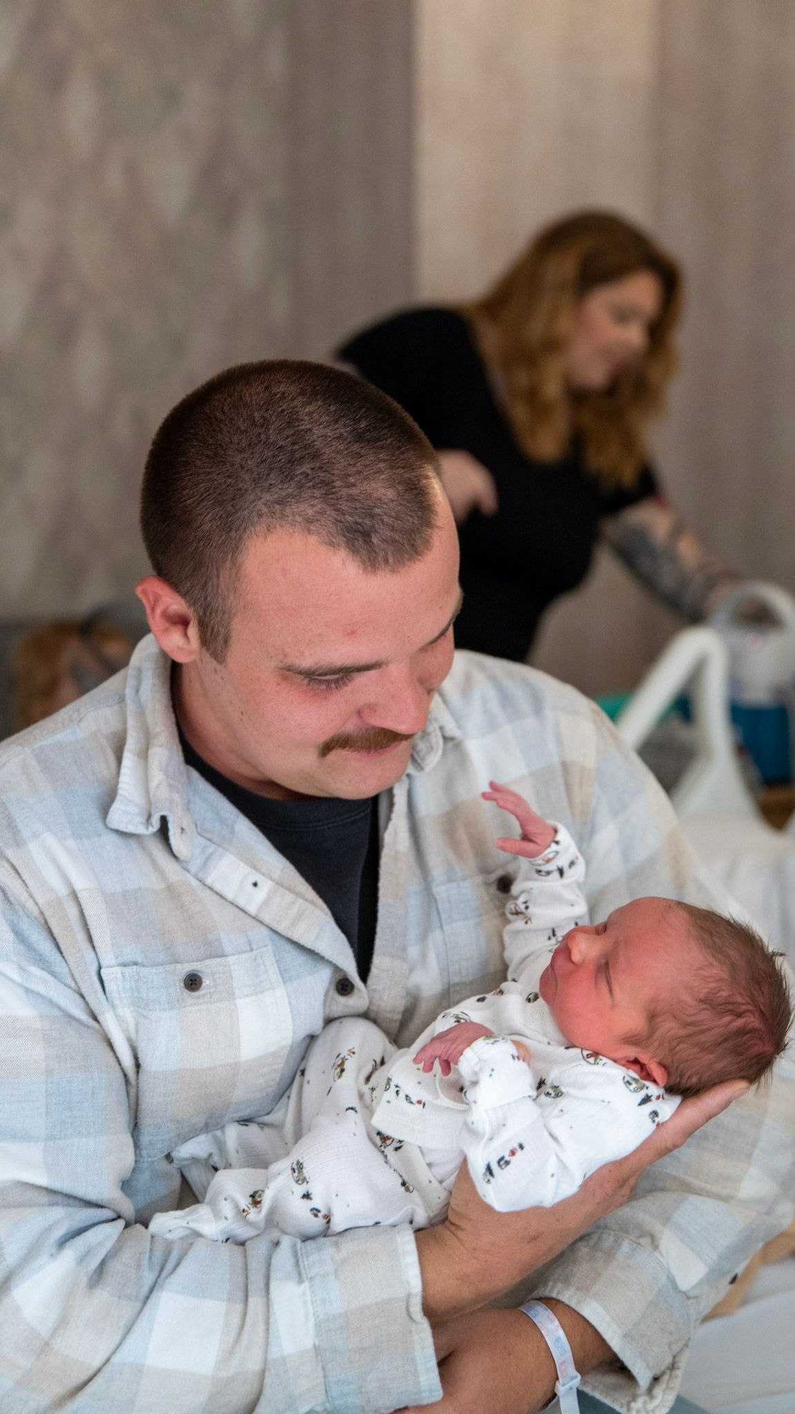 A parent in a light colored shirt tenderly holds and gazes at their newborn baby wrapped in white.