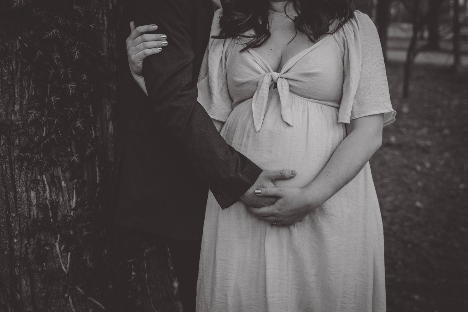 A black and white maternity photo showing a couple's tender moment outdoors.