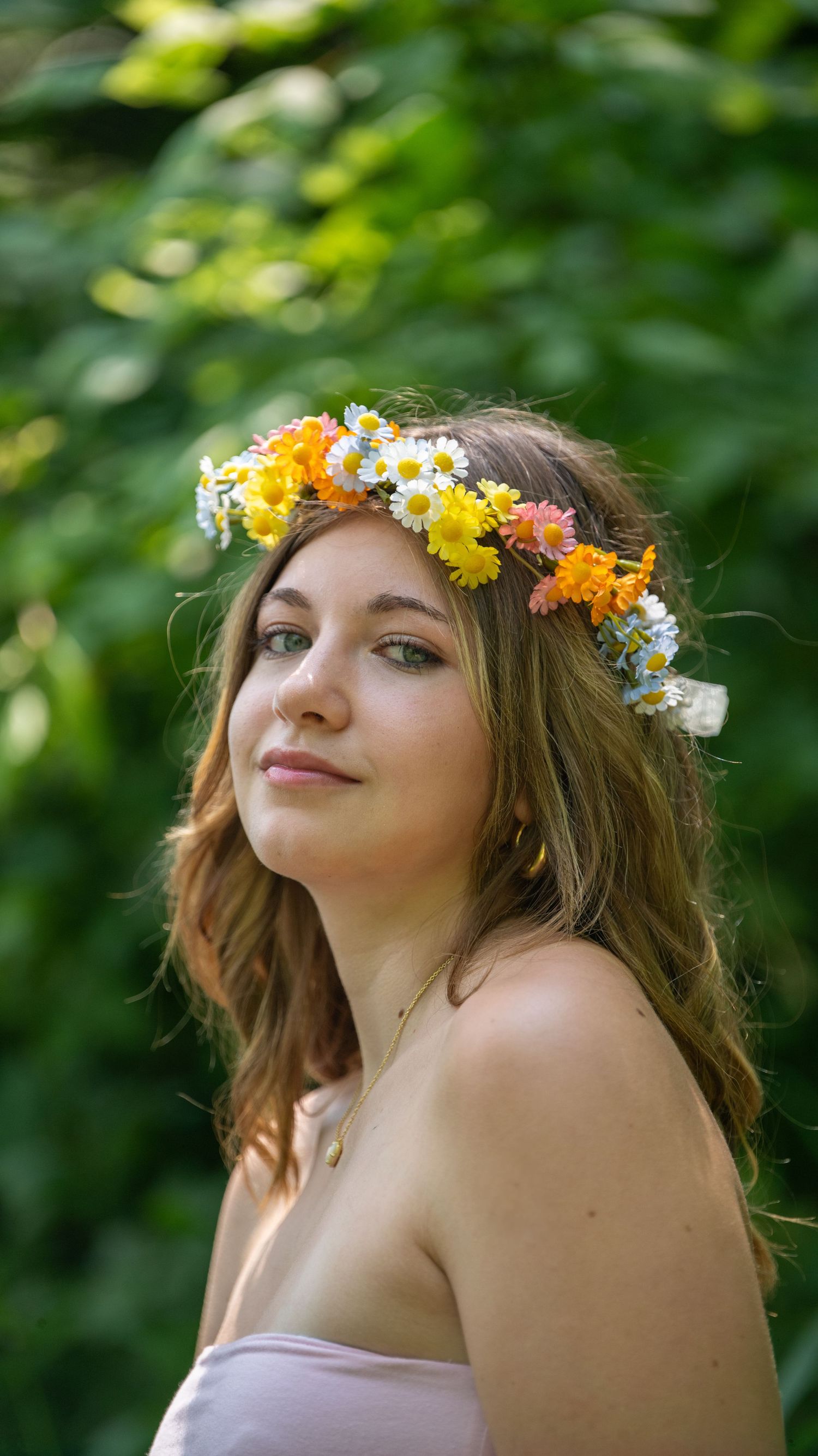Person wearing flower crown with yellow daisies and white flowers against green foliage.