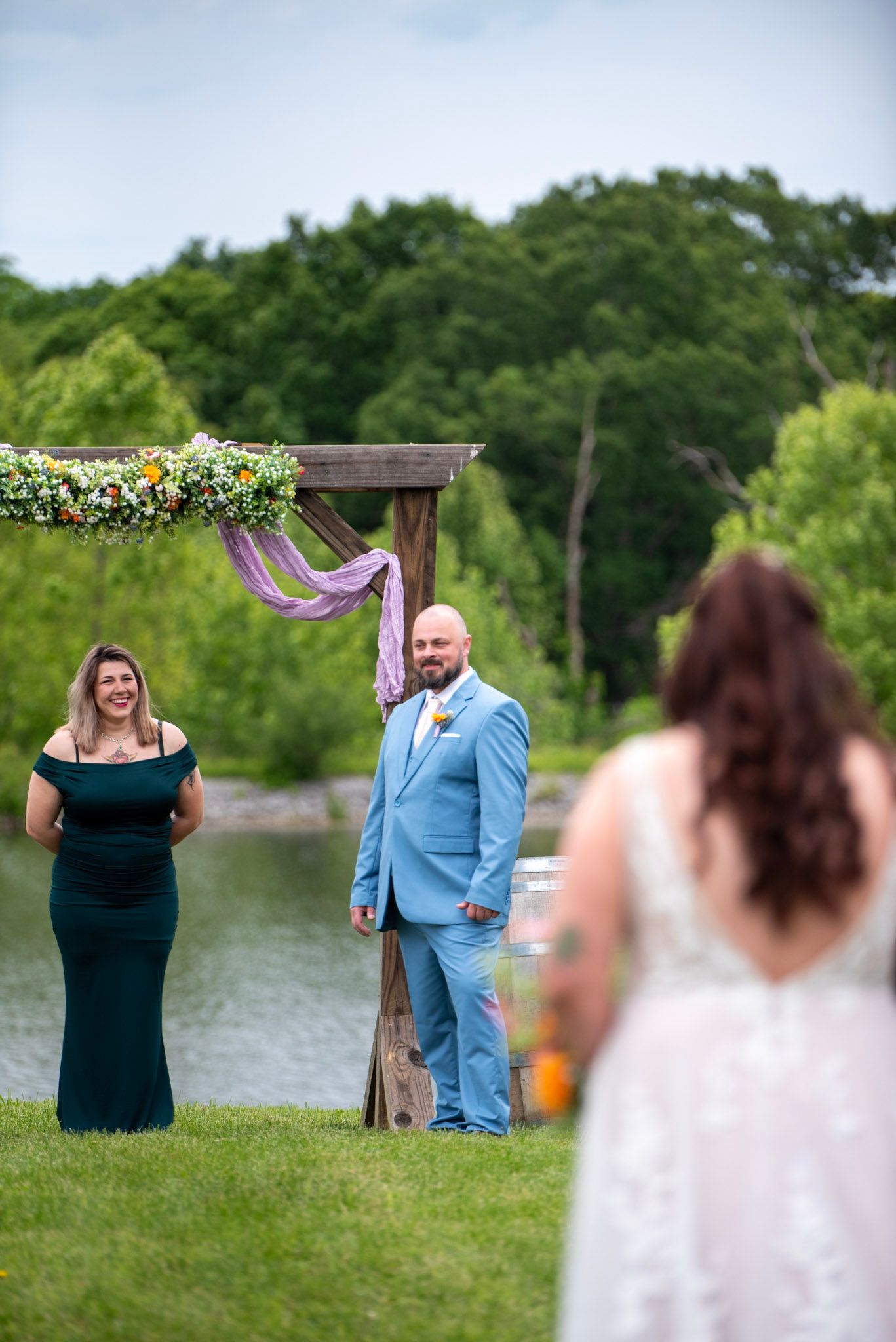An outdoor wedding ceremony setup with a wooden arch decorated in flowers and purple ribbons.