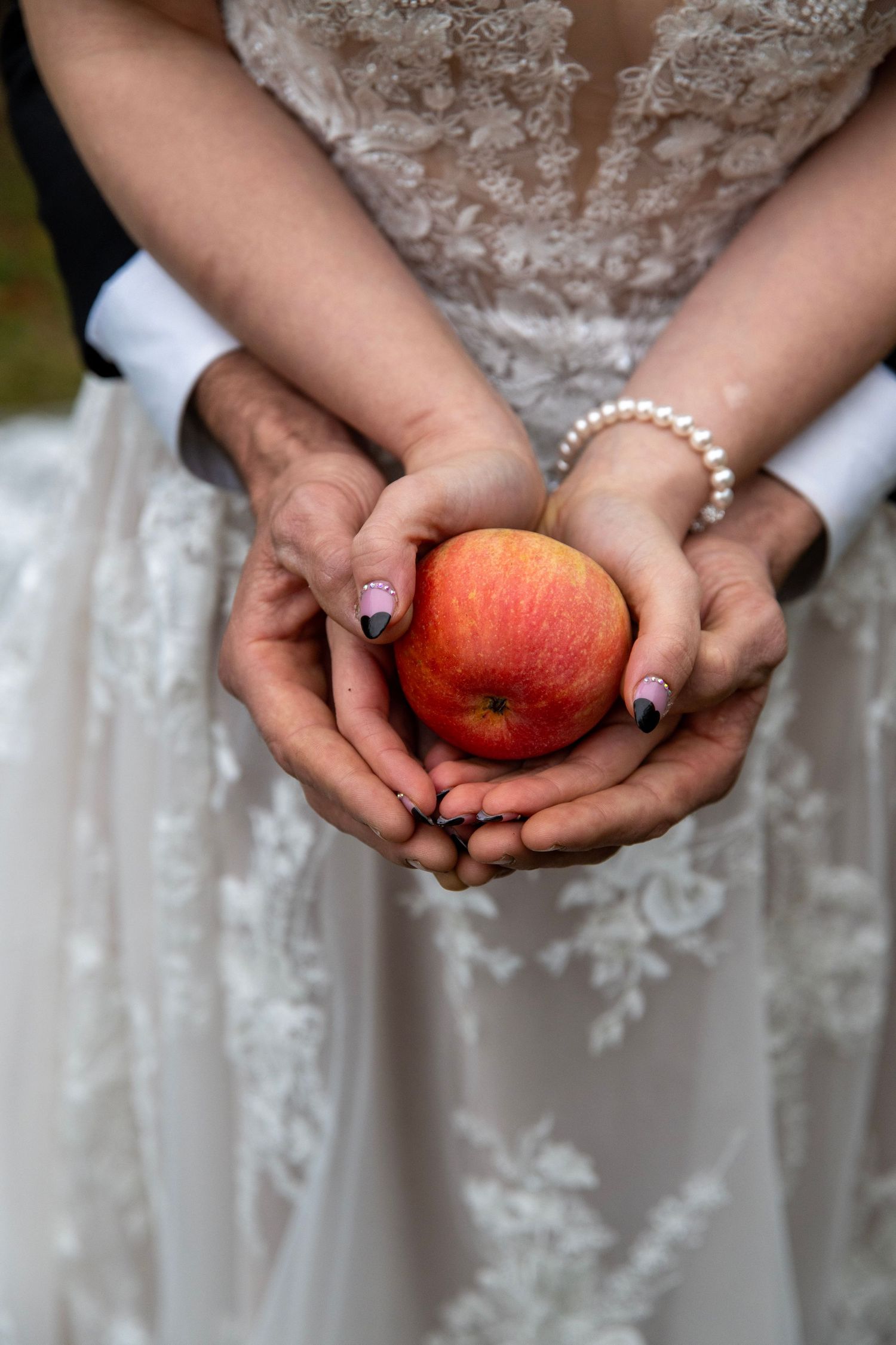 Close-up of hands in white lace dress holding a red apple.