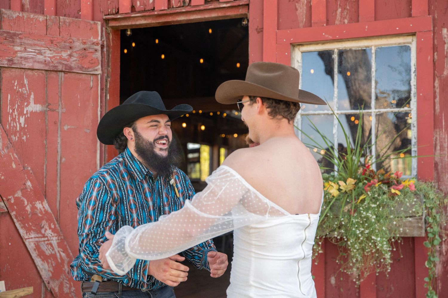 Wedding couple shares intimate moment in front of rustic red barn during sunset.