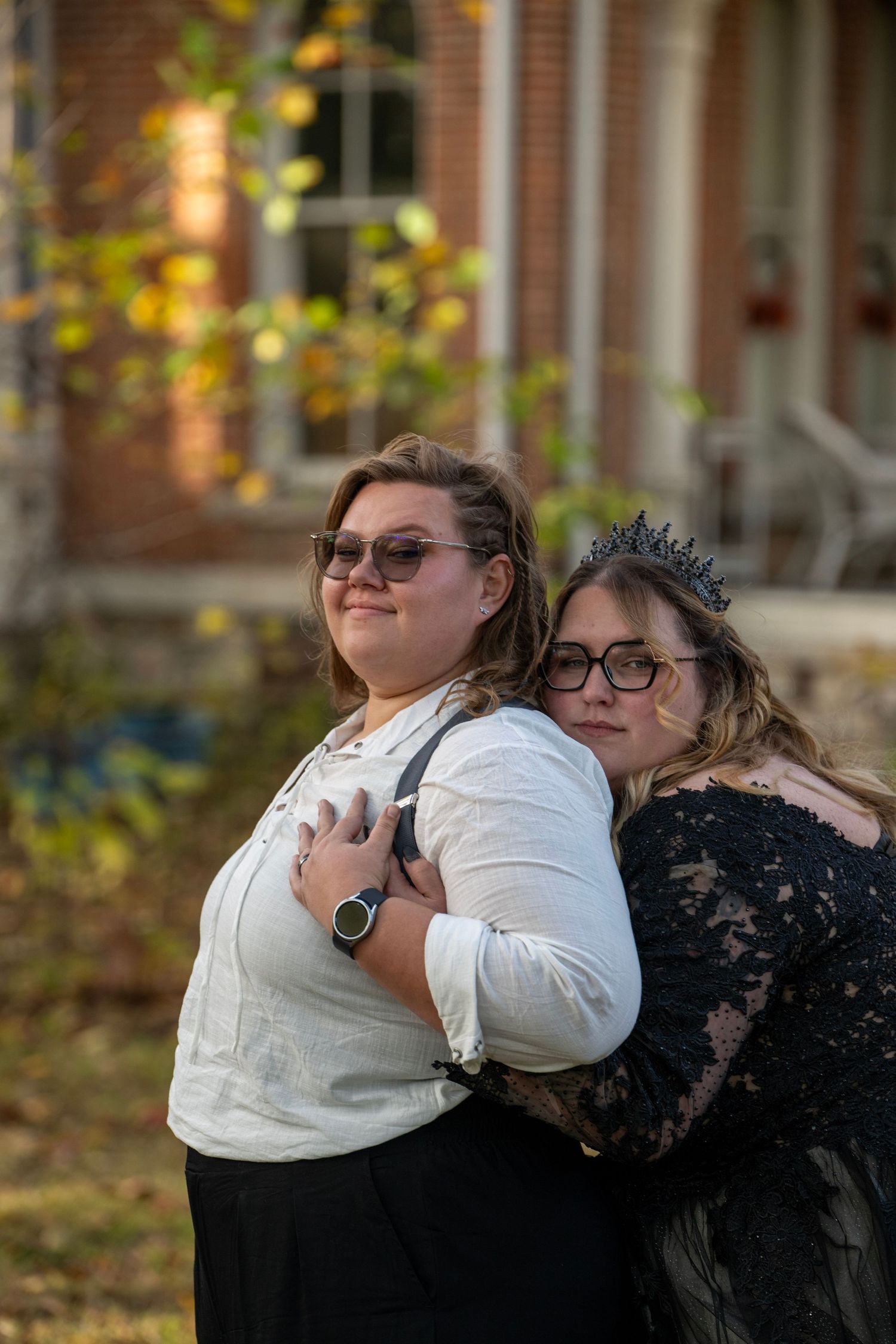 Two people share a tender moment in front of a historic brick building during autumn.