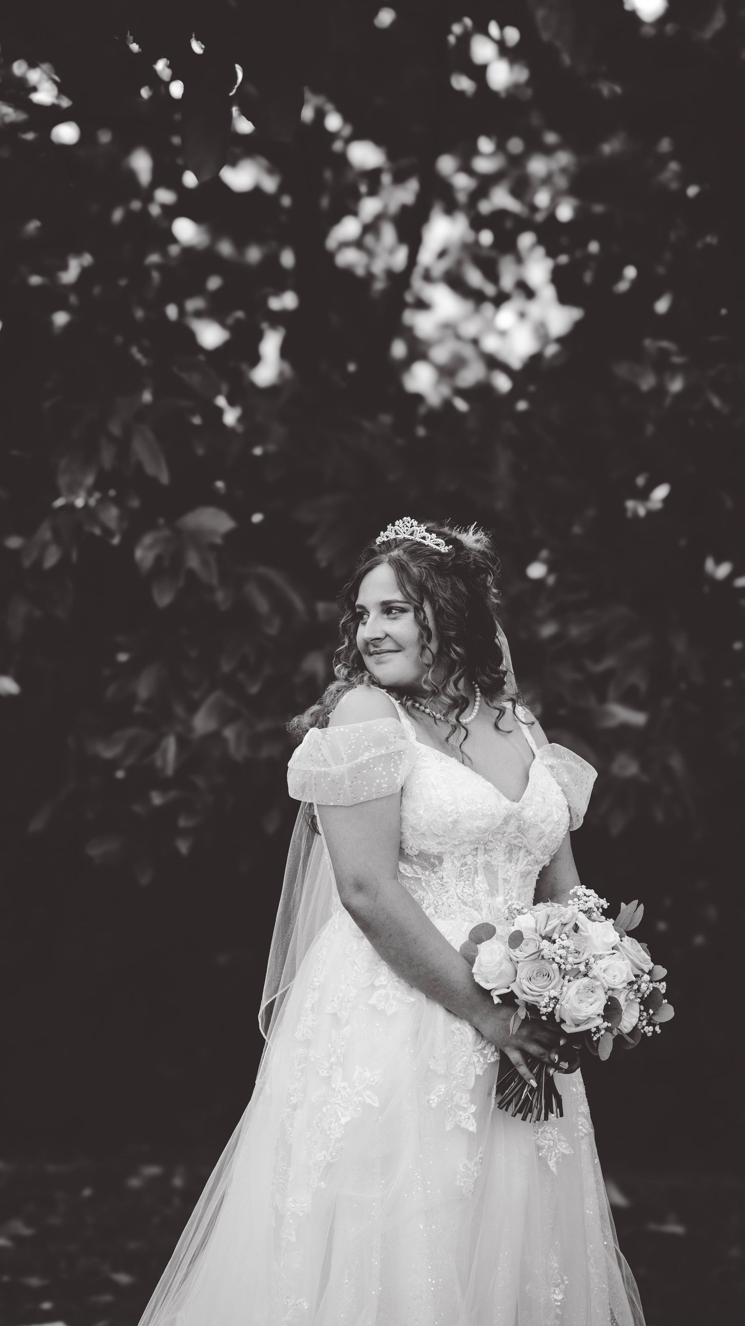 Bride in a white lace gown holds a bouquet during an emotional outdoor wedding moment.