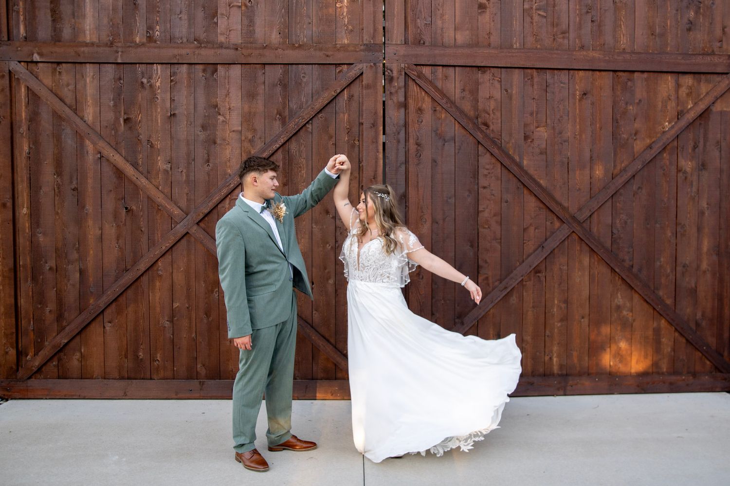 A playful wedding couple posing in front of rustic wooden barn doors.