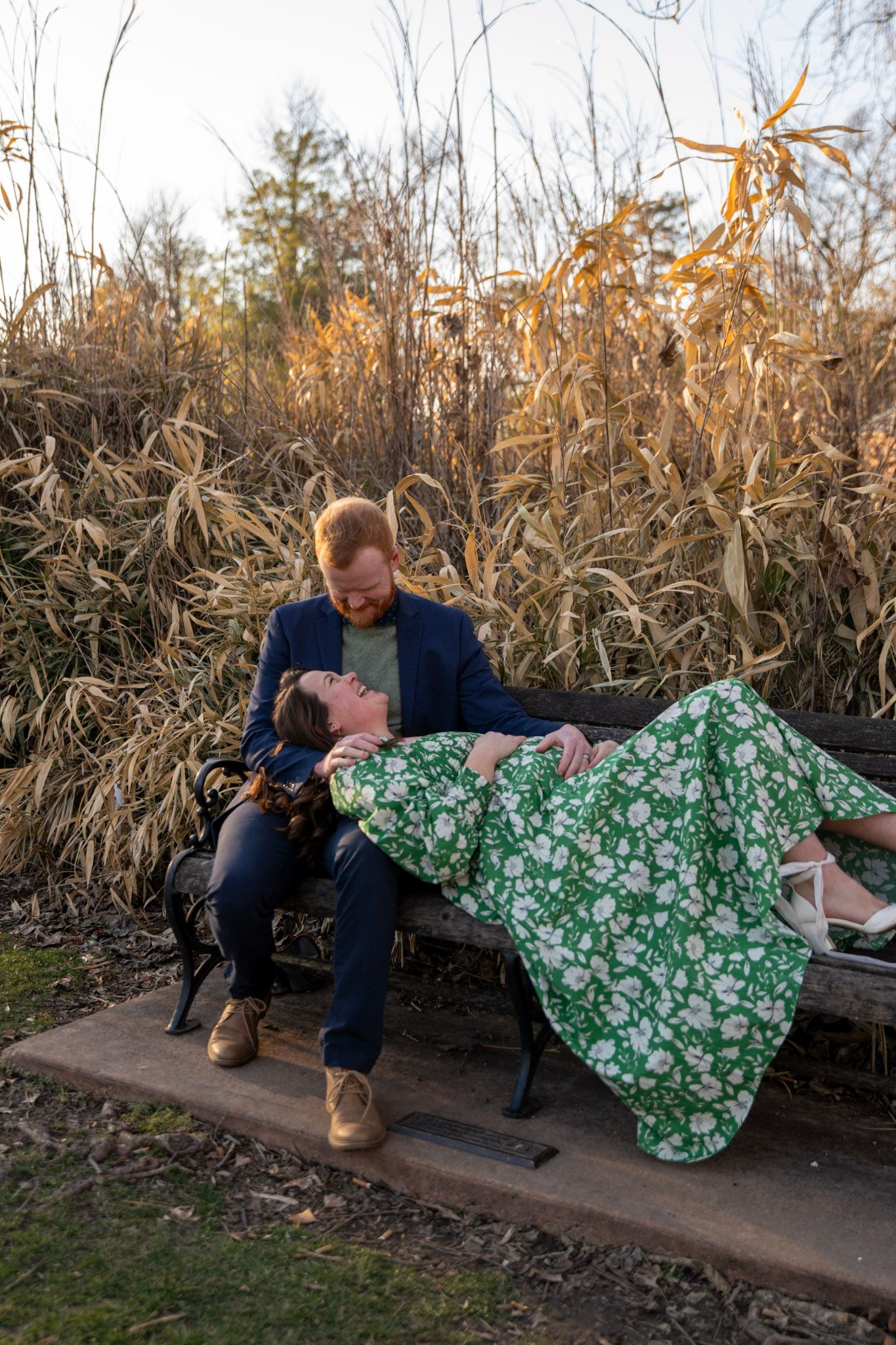 Couple poses playfully on a wooden bench surrounded by dried corn stalks at sunset.