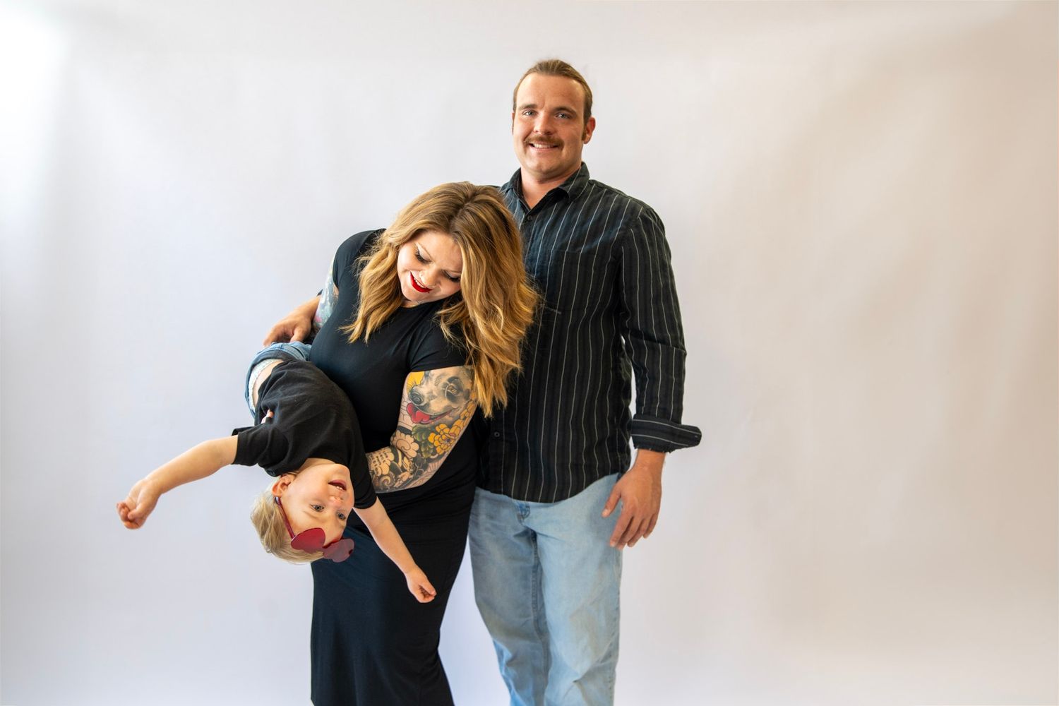 Playful couple posing together during pregnancy photo session against white background.