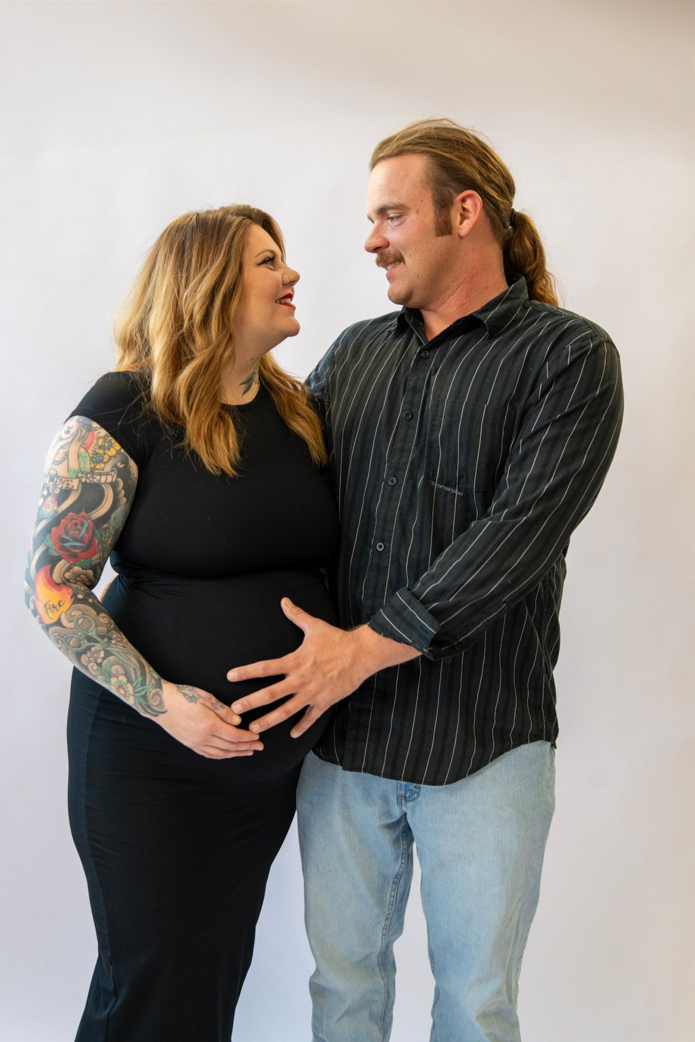 Loving couple sharing tender moments during pregnancy photoshoot against white backdrop.