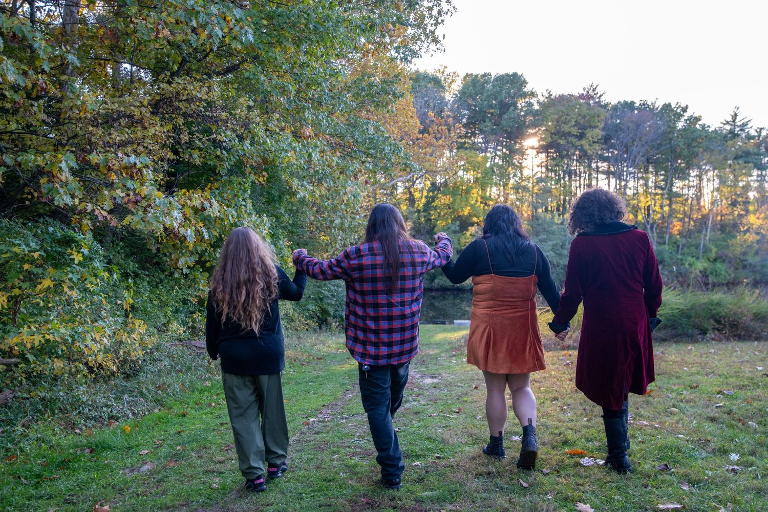 Several people walking along a grassy path with trees showing fall colors in the distance.