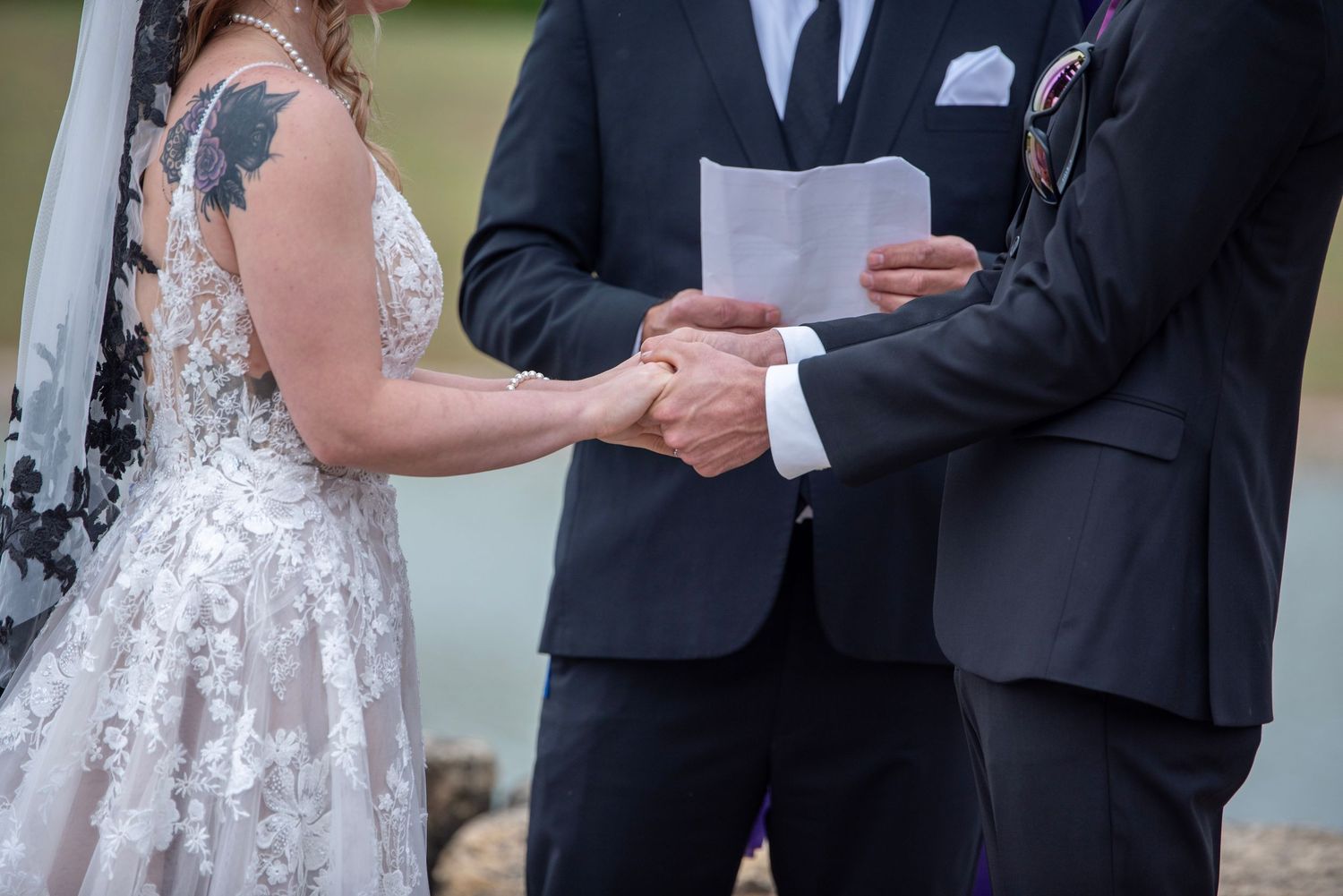 Close-up of couple holding hands during outdoor wedding ceremony.