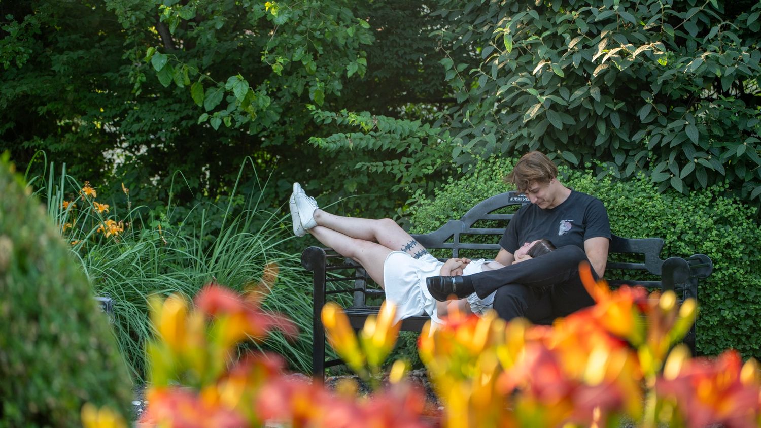 A couple relaxes among colorful flowers in a lush garden setting.