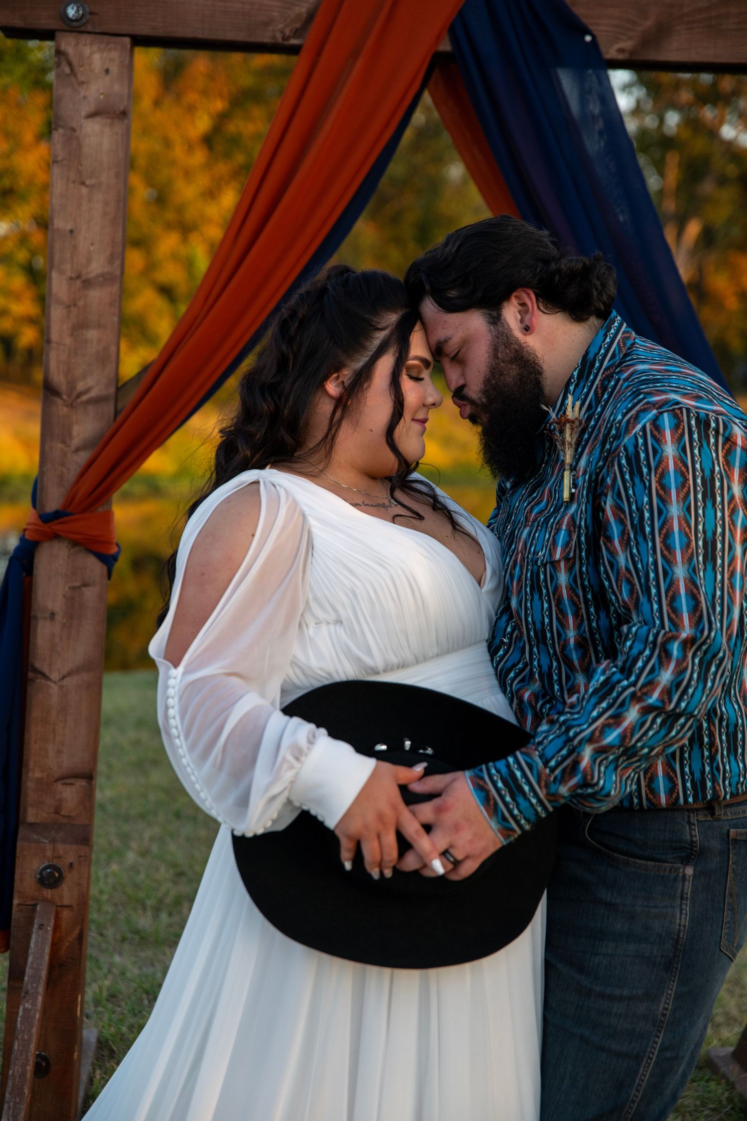 Romantic moment captured under wooden arch with navy and rust drapery at sunset.