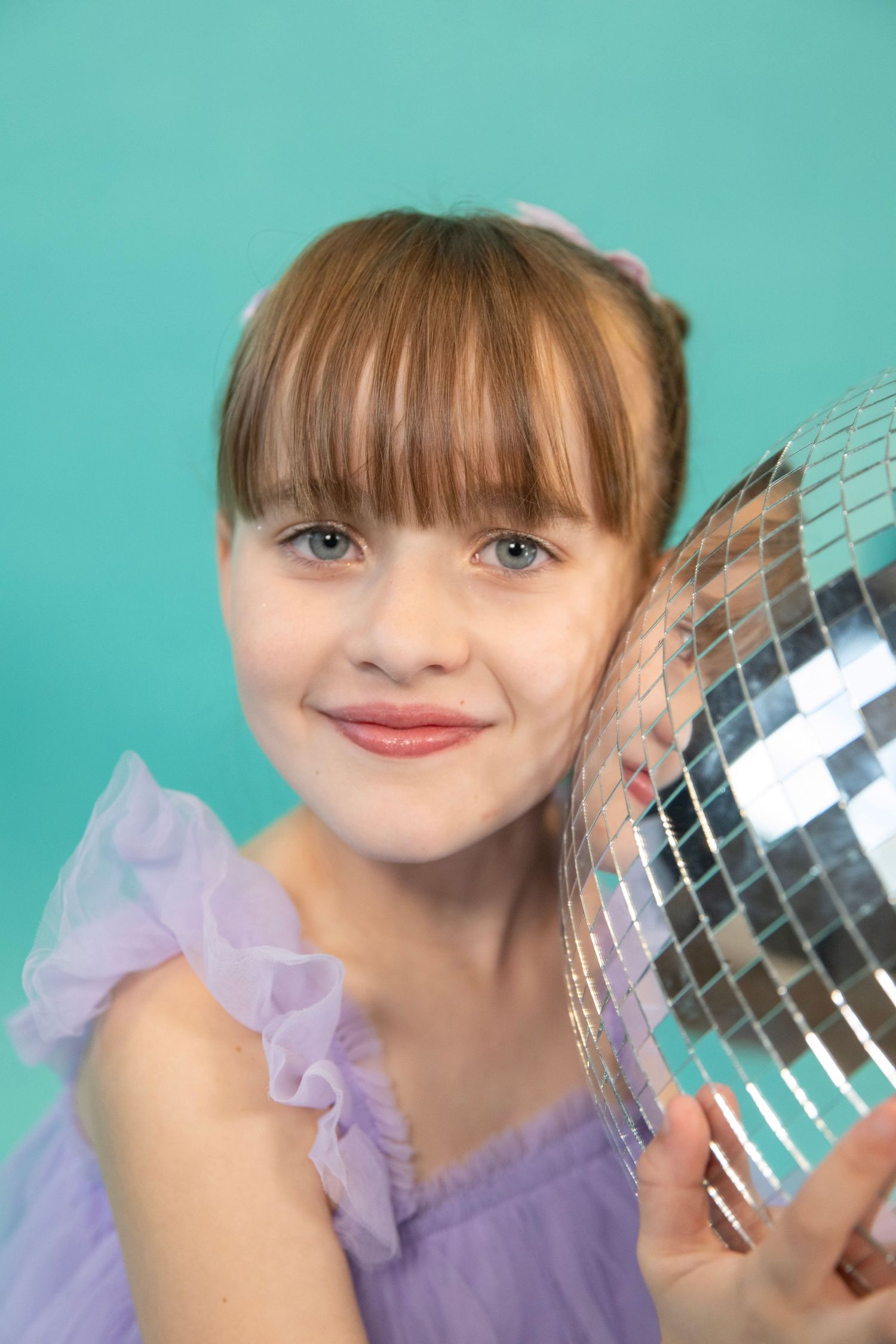 Studio portrait with disco ball against turquoise background.