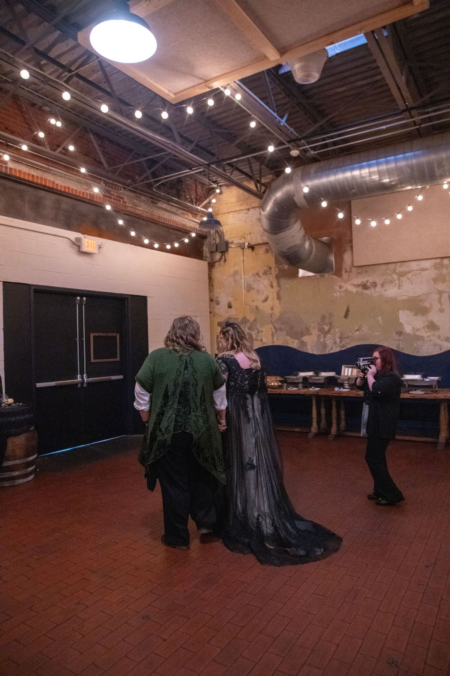 People in gothic attire standing near a decorated table at an indoor event space.