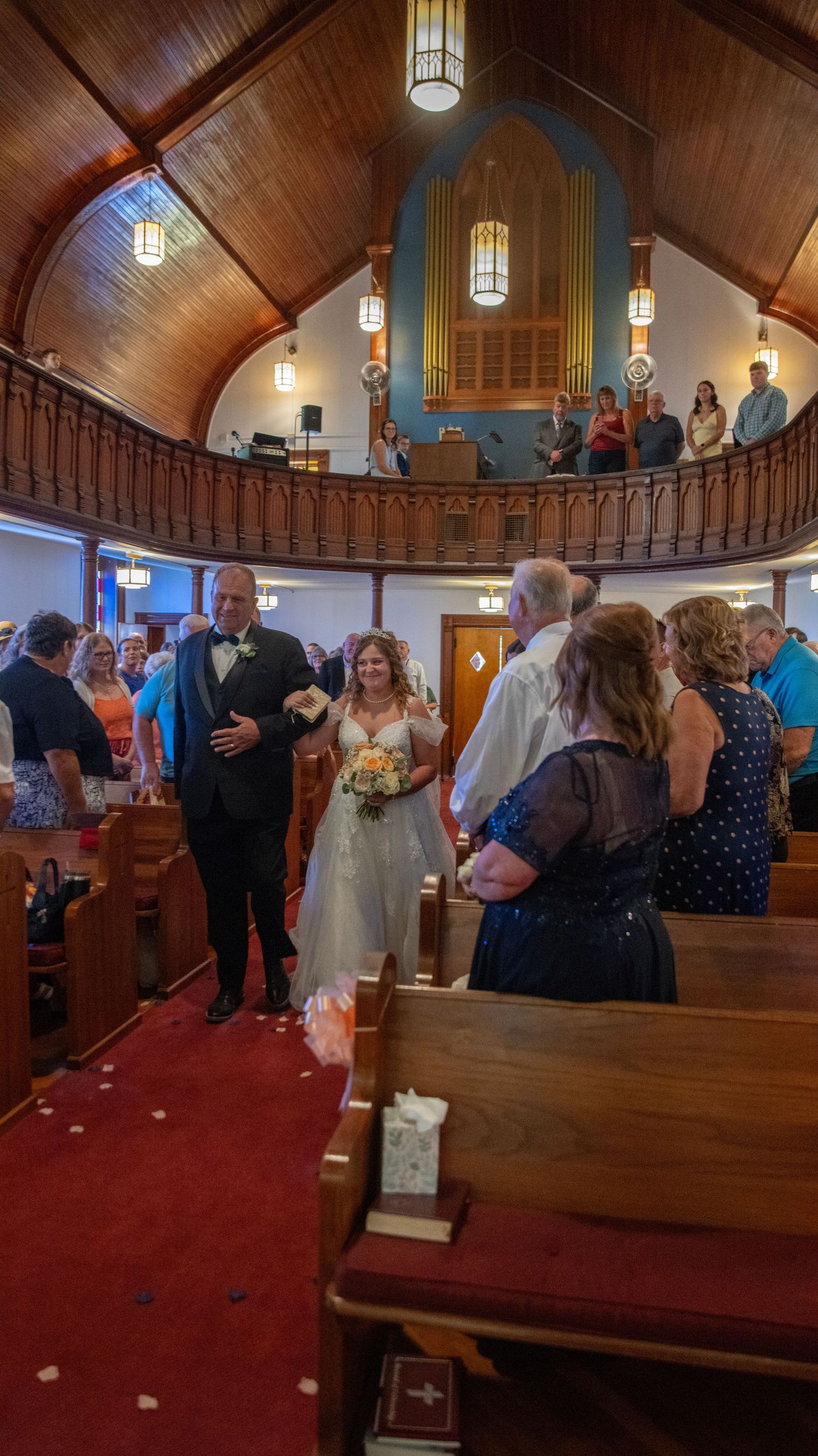 Wedding ceremony in progress inside a church with wooden vaulted ceiling and pews.
