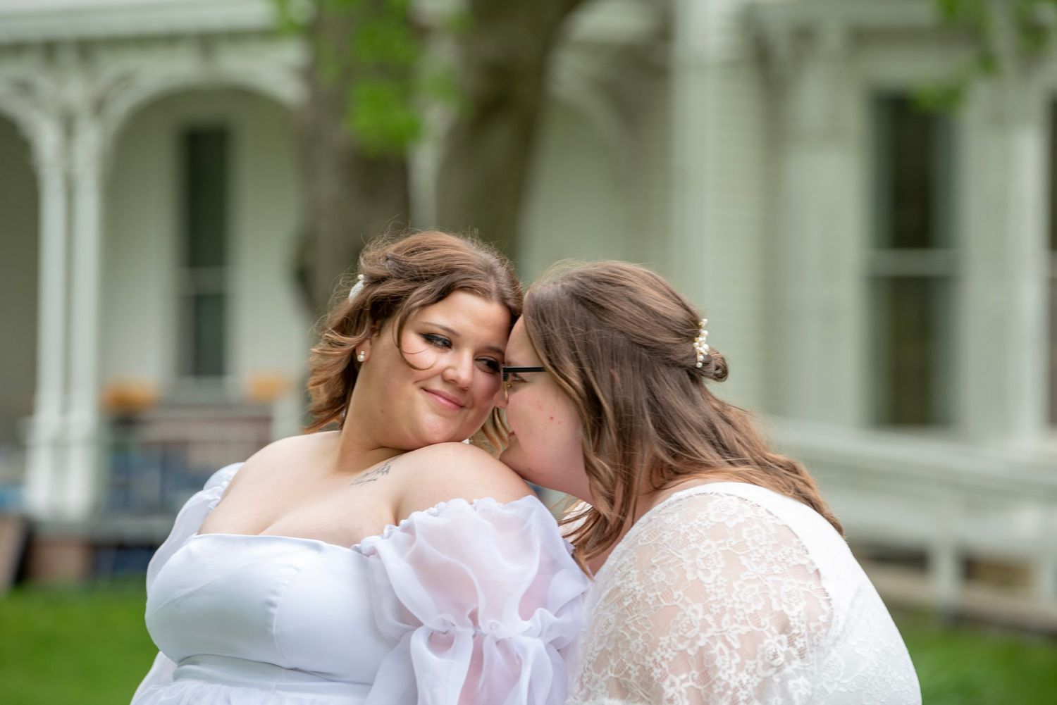 Couple in white wedding dresses embracing in front of a historic building.