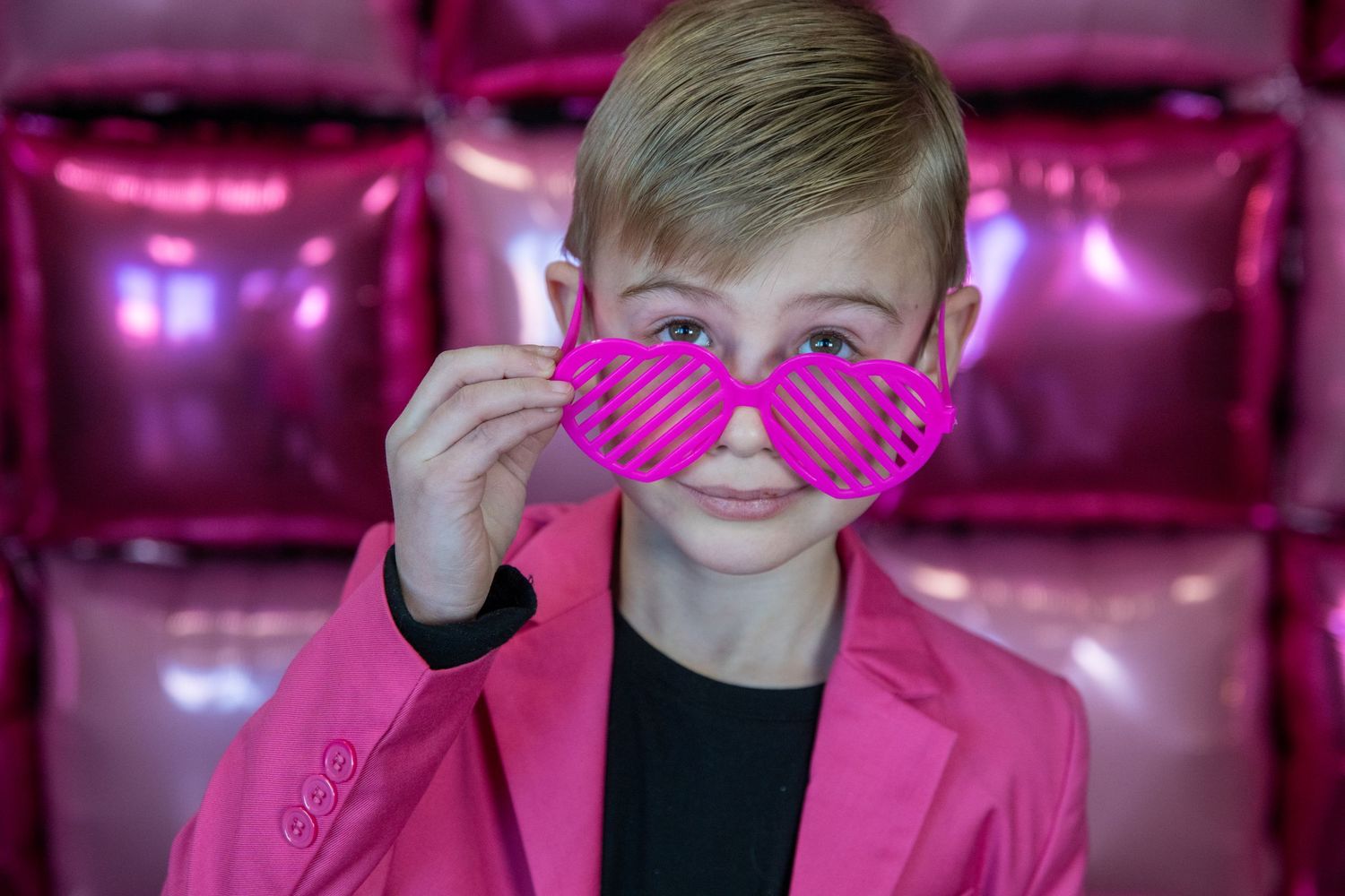 Fun poses with pink heart-shaped glasses against a shimmery pink backdrop.