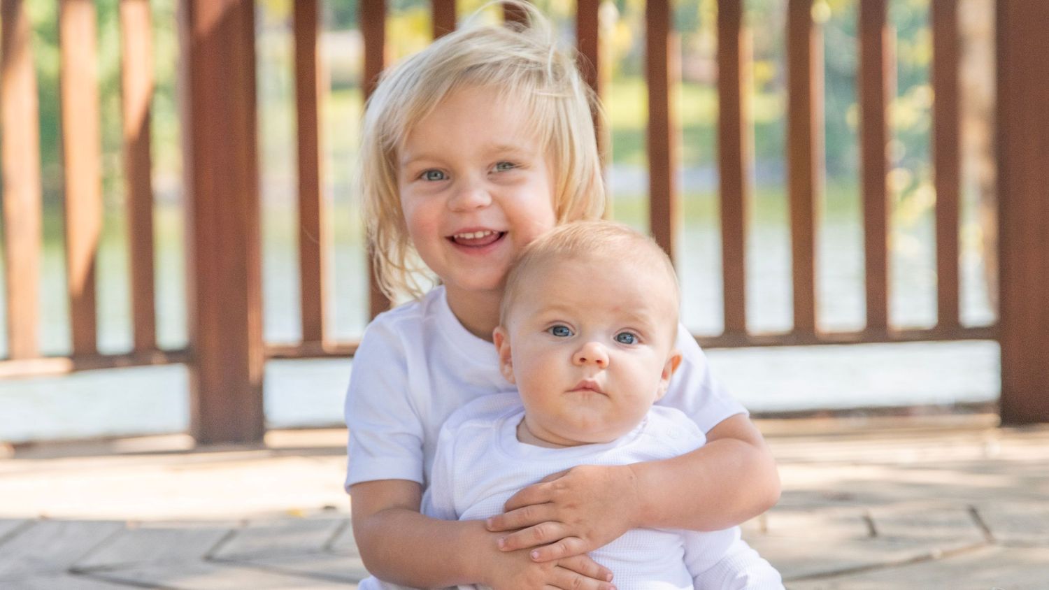 Sweet sibling moments photographed in natural light on a wooden deck.