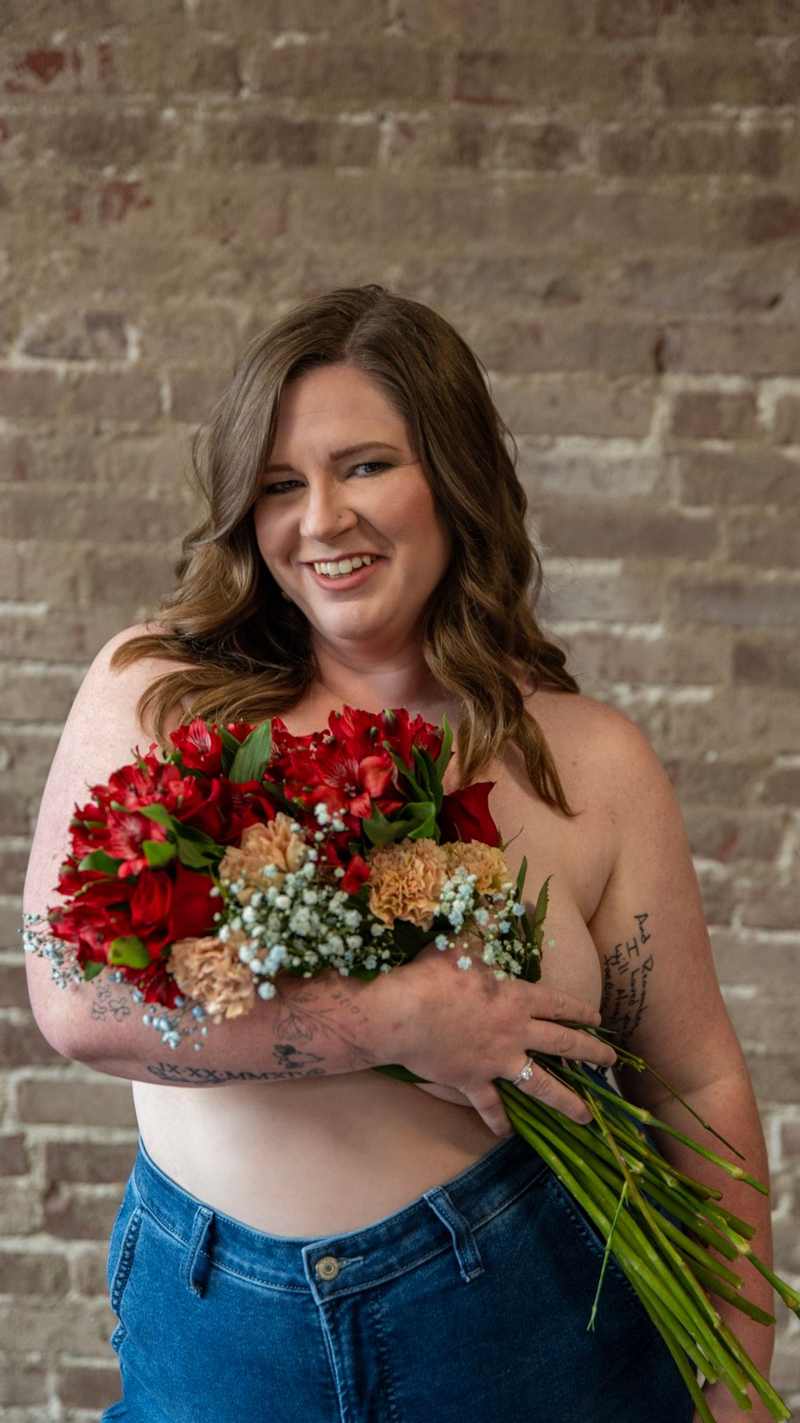 Artistic portrait against textured wallpaper holding red and peach floral bouquet.