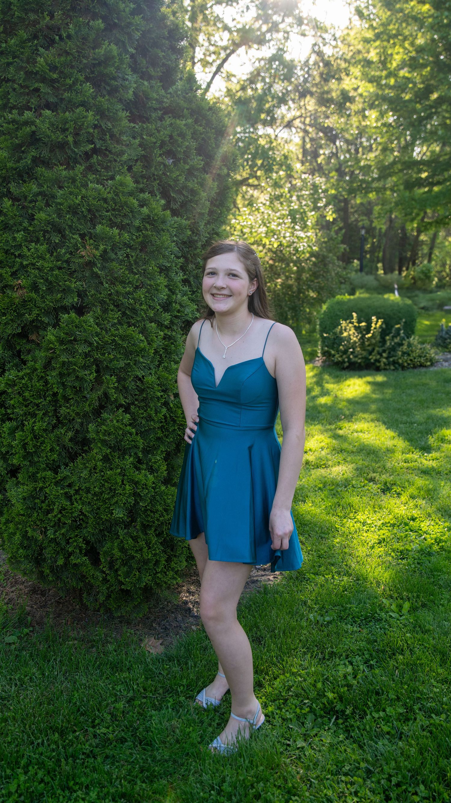 Summer portrait series in a blue dress with sunlit greenery and hedges in the background.