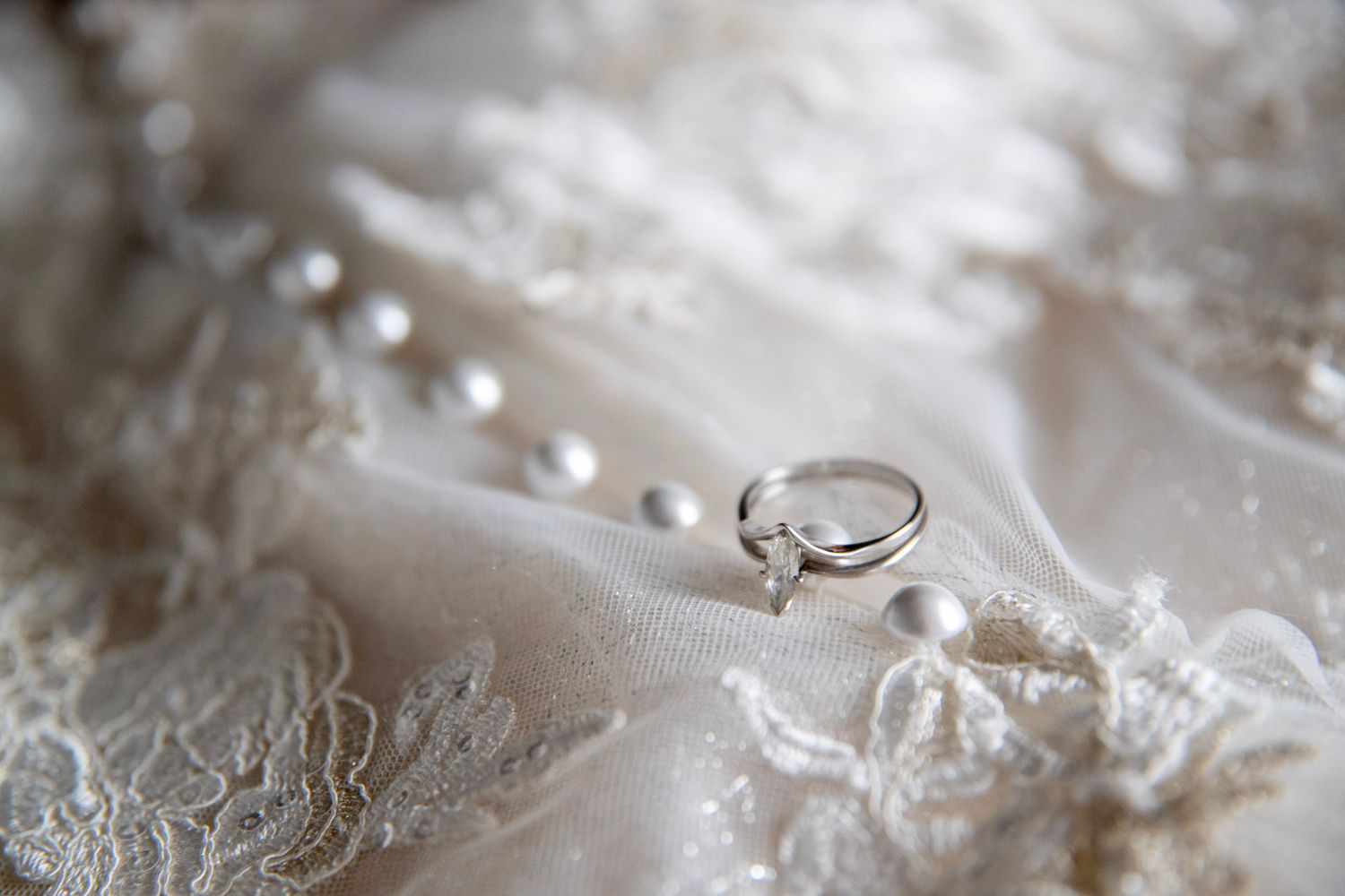 Close-up detail shots of wedding rings and lace on white fabric.