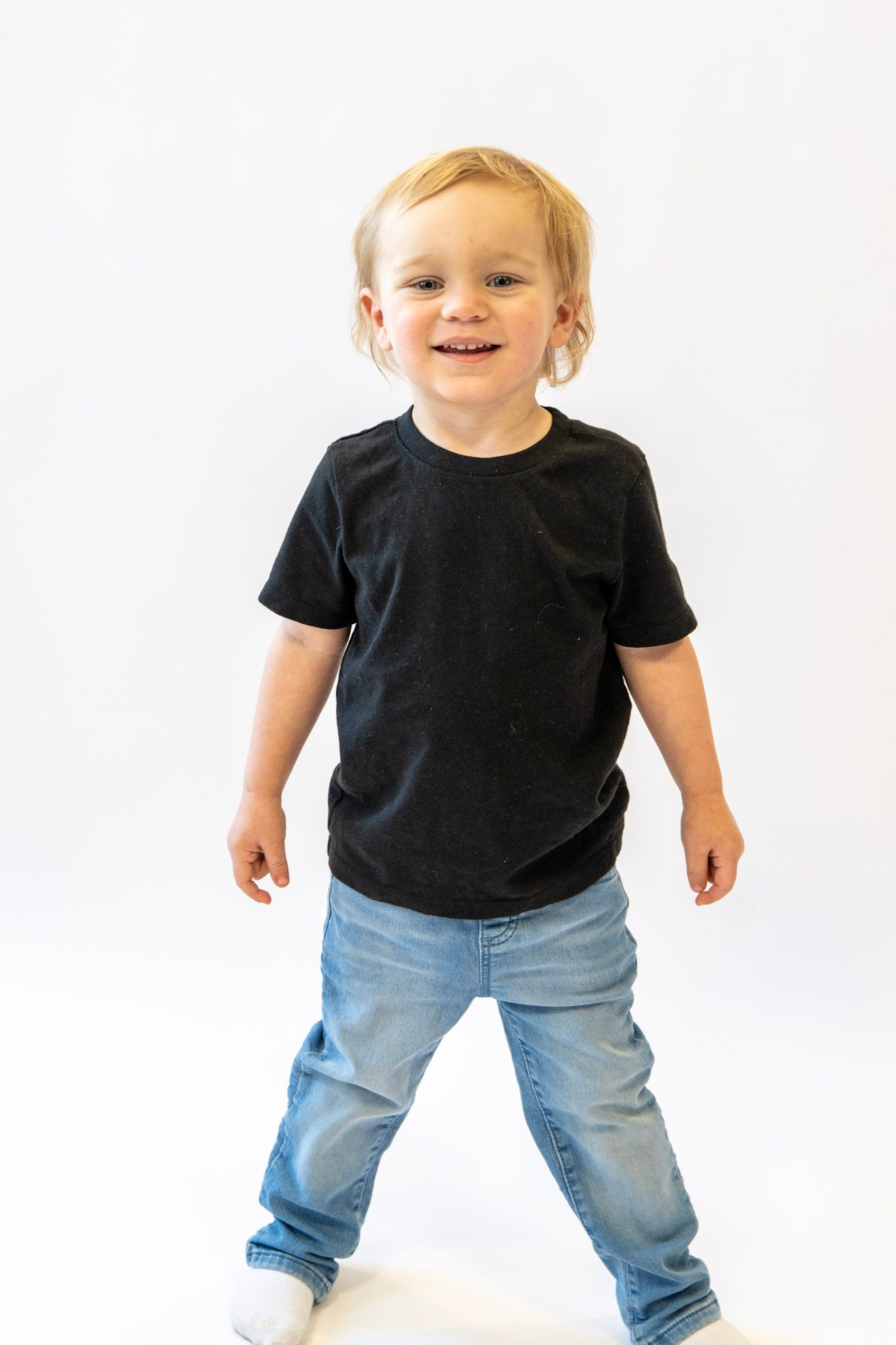 Happy toddler in black shirt and jeans playing against white background.