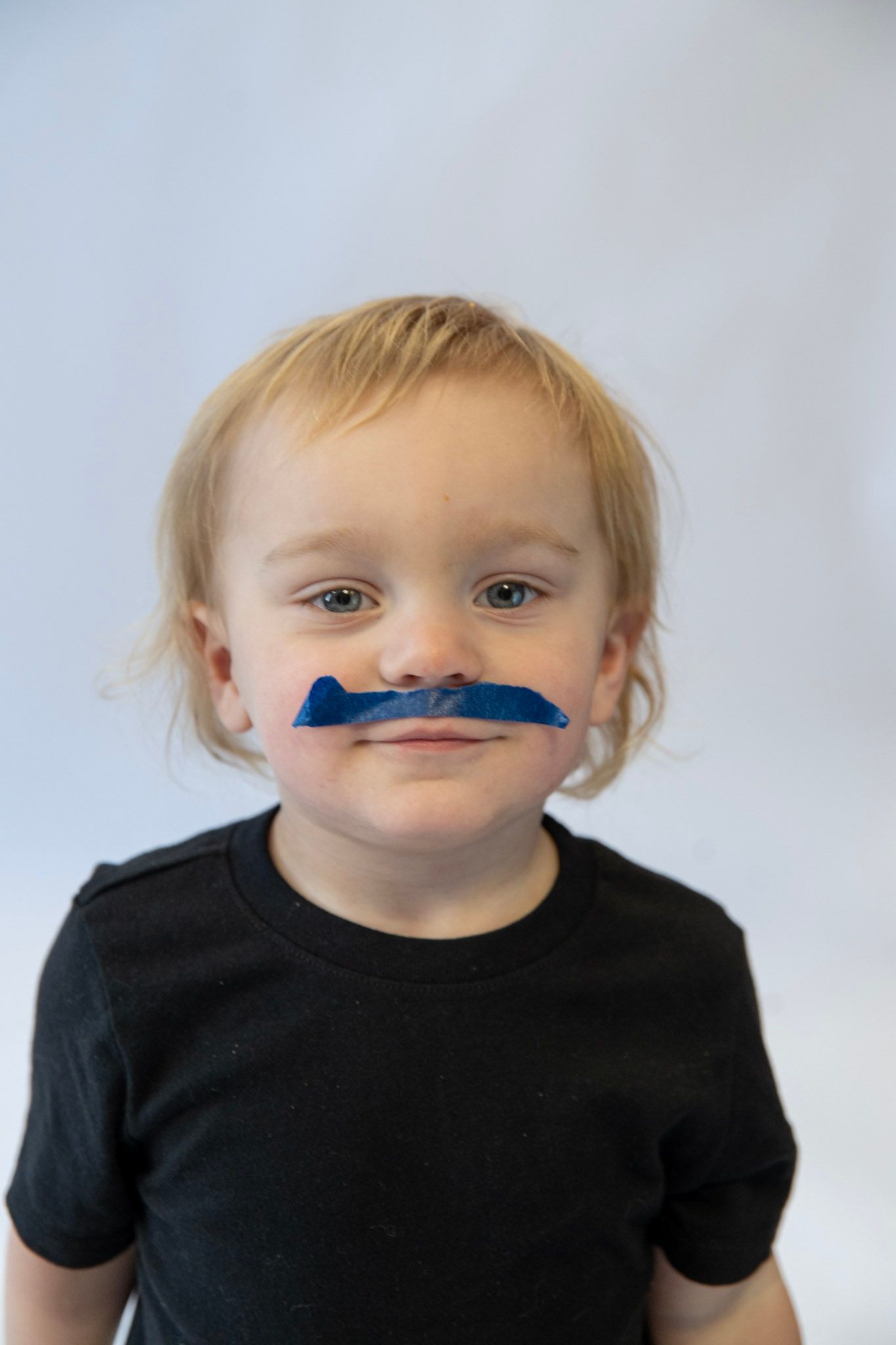 Child in black shirt making silly faces at camera against white background.
