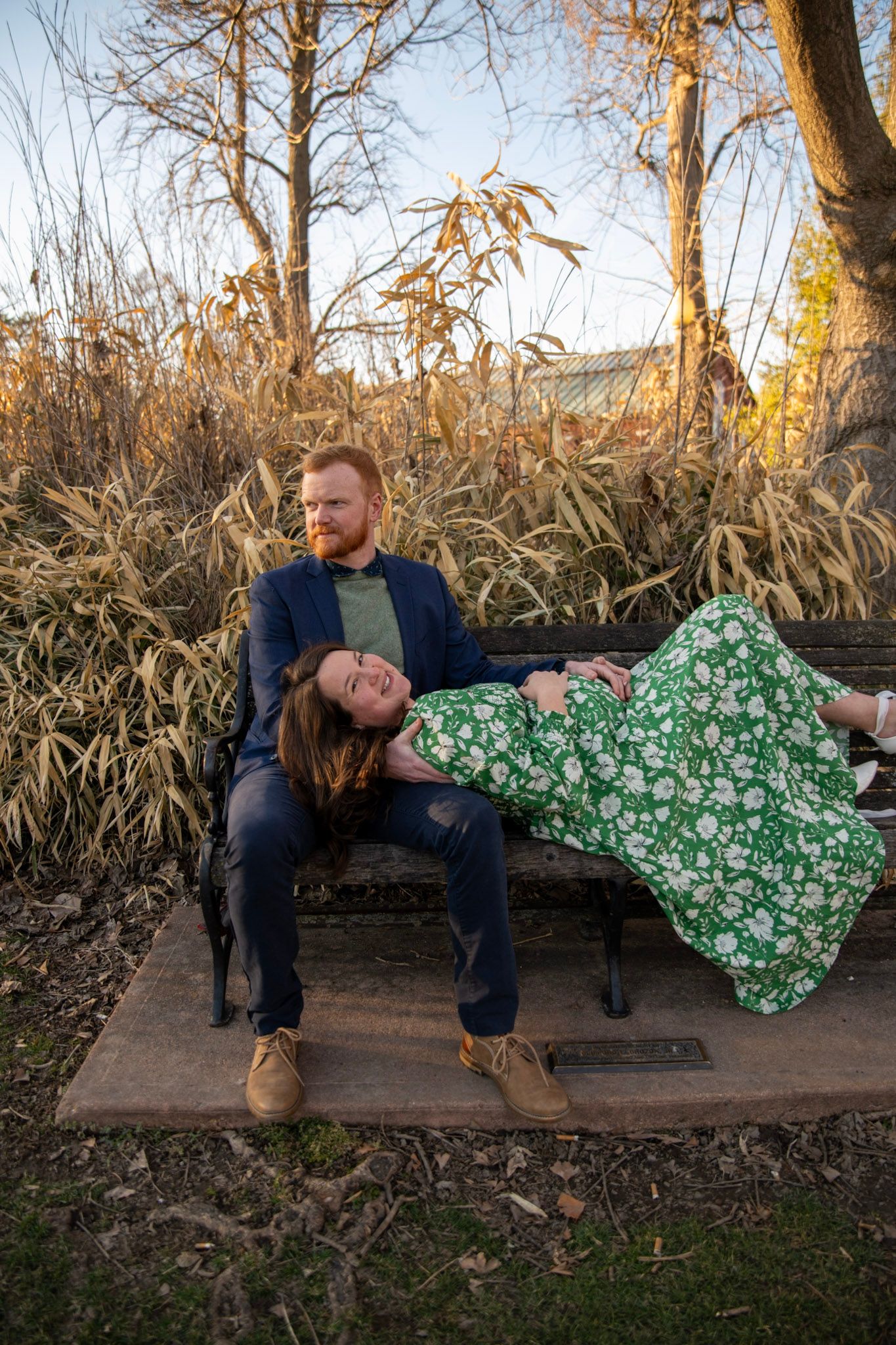 Couple shares intimate moment on rustic wooden bench with cornfield backdrop at sunset.