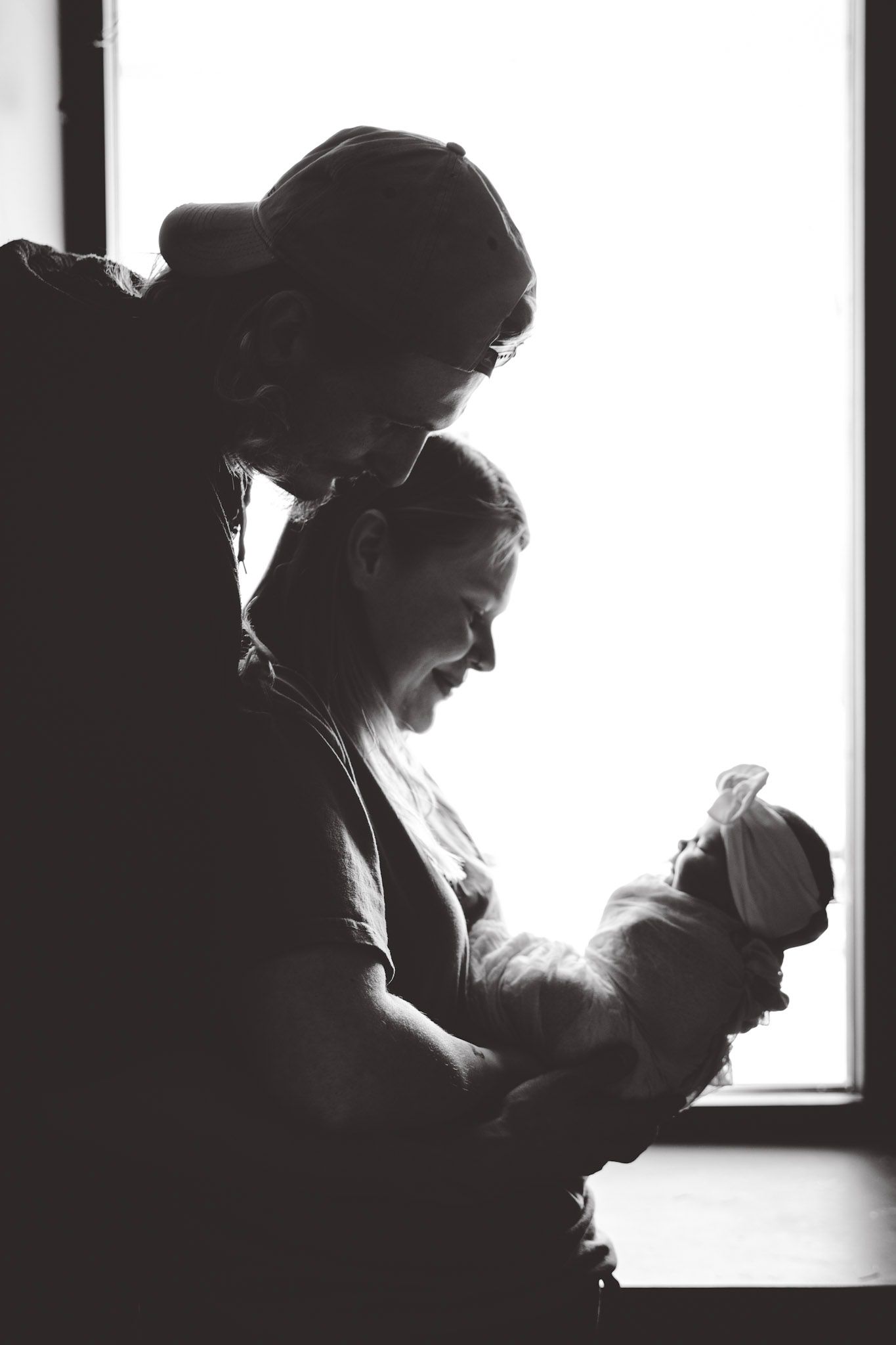 Silhouette of parent and baby in window light creating dramatic black and white portrait.