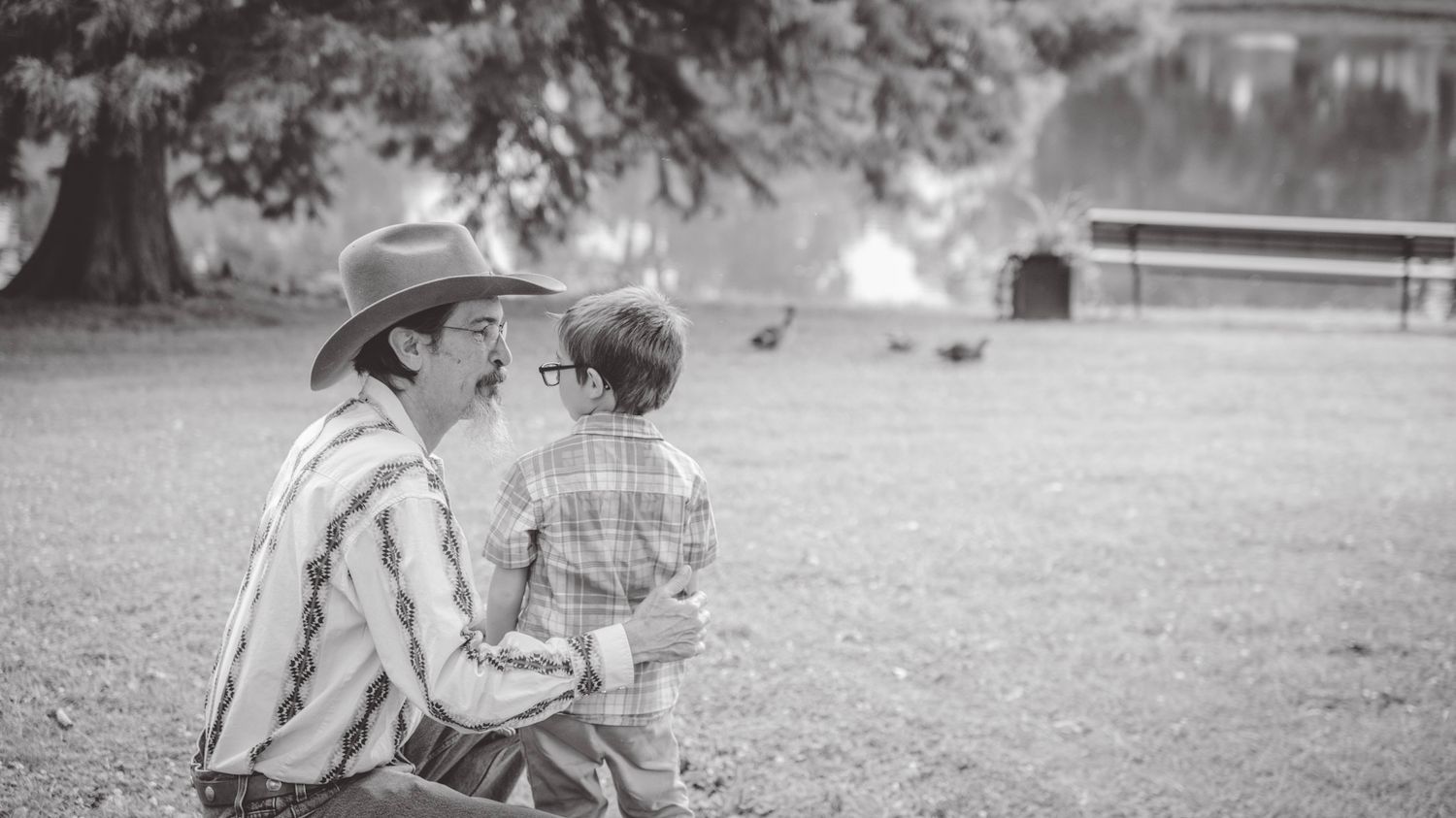 A black and white portrait captures two figures sharing a moment by a pond.