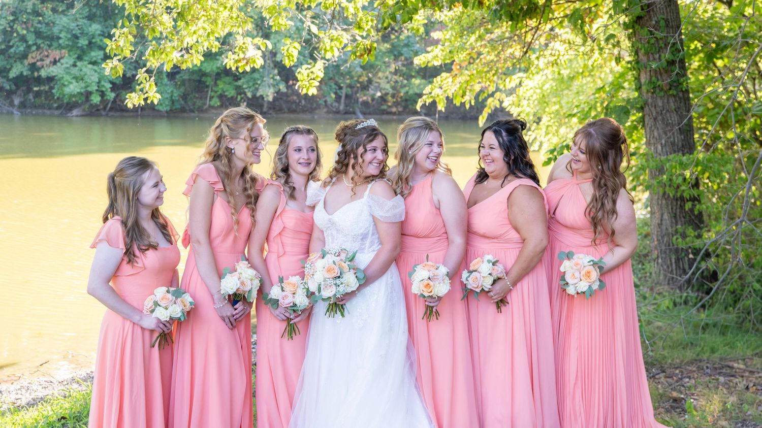 Bridesmaids in coral dresses stand with bride for outdoor wedding photos.