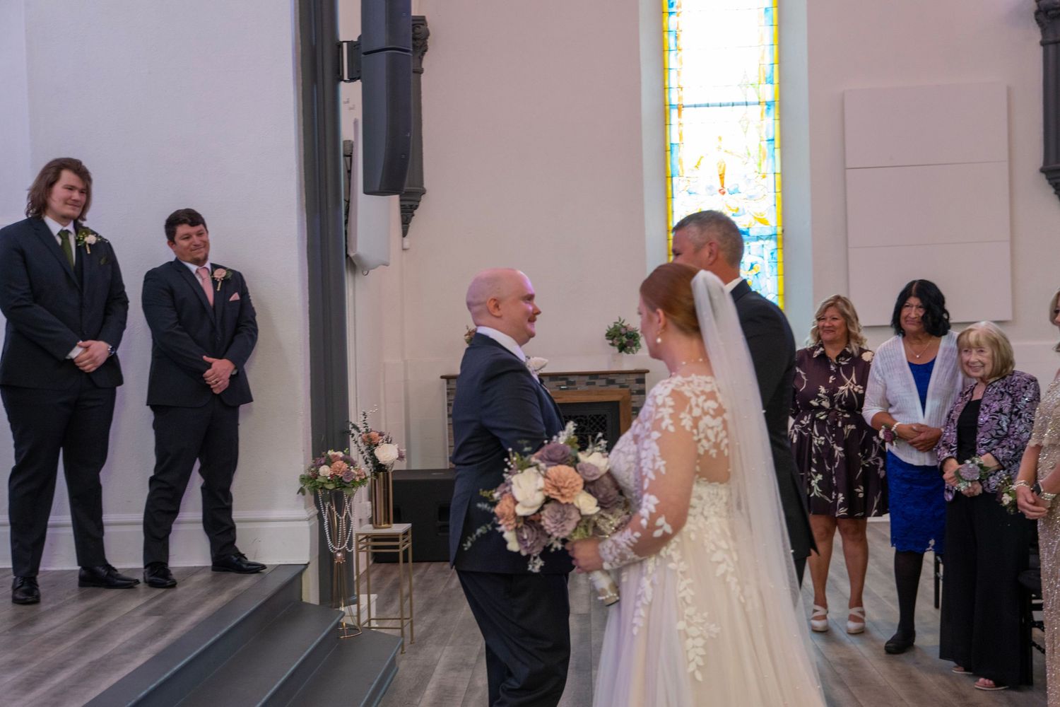 Wedding ceremony proceedings in a bright church with stained glass windows.