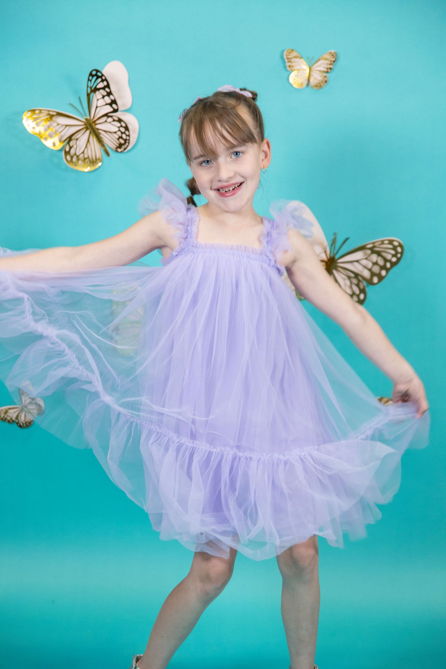 Dreamy dance pose in a purple tulle dress with butterfly accents on aqua background.