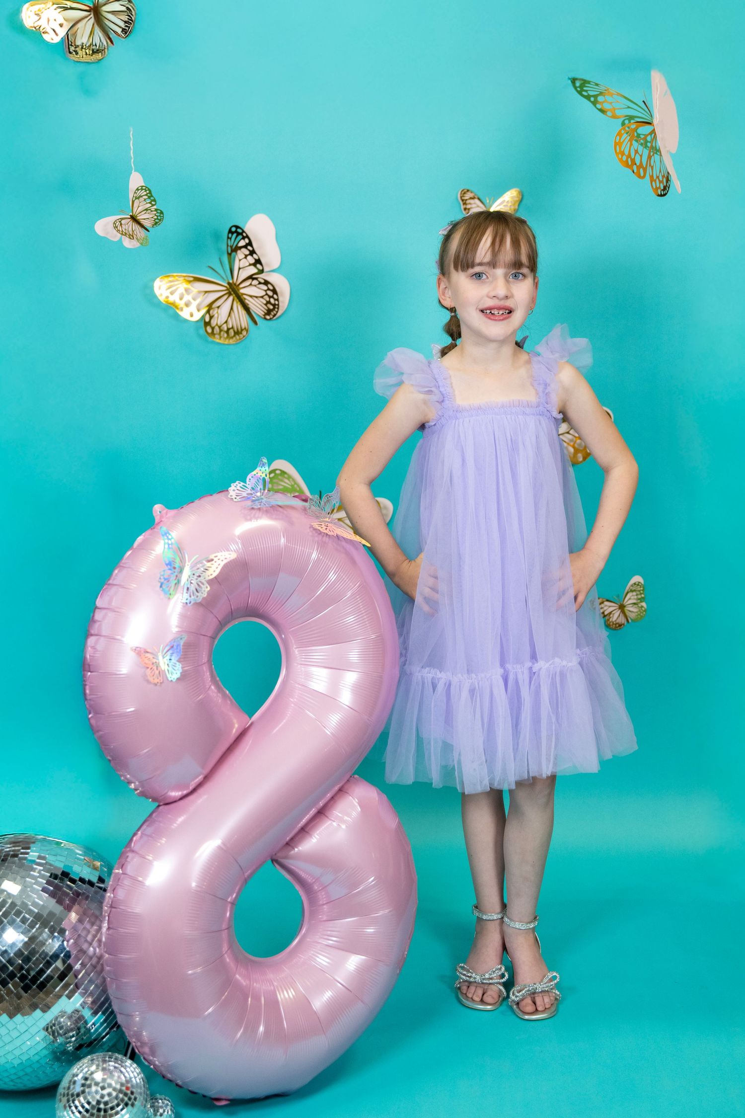 Pink number 2 balloon decoration with butterflies and a purple tulle dress against turquoise backdrop.