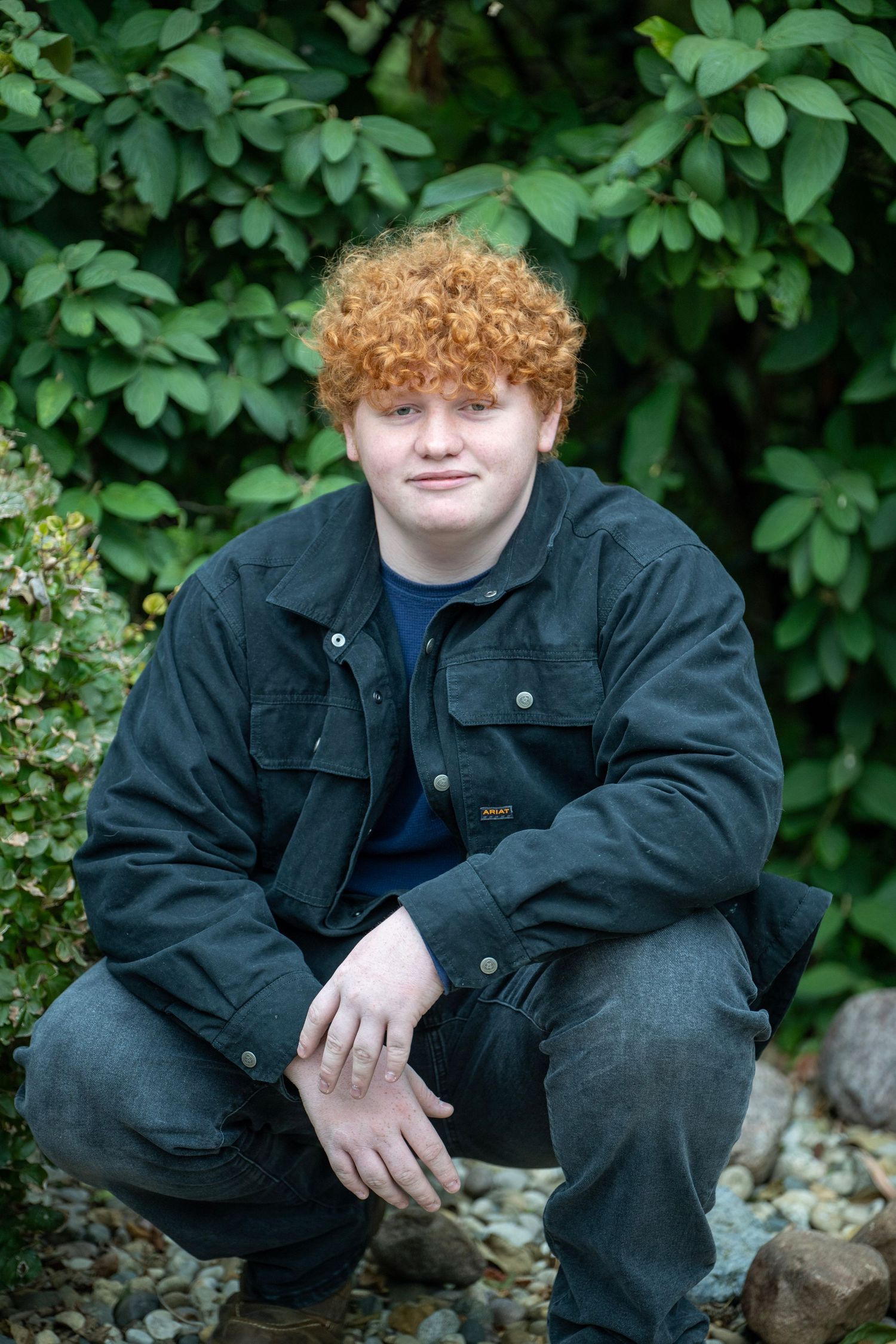 Outdoor portrait series with green foliage backdrop showing relaxed poses on rocks.