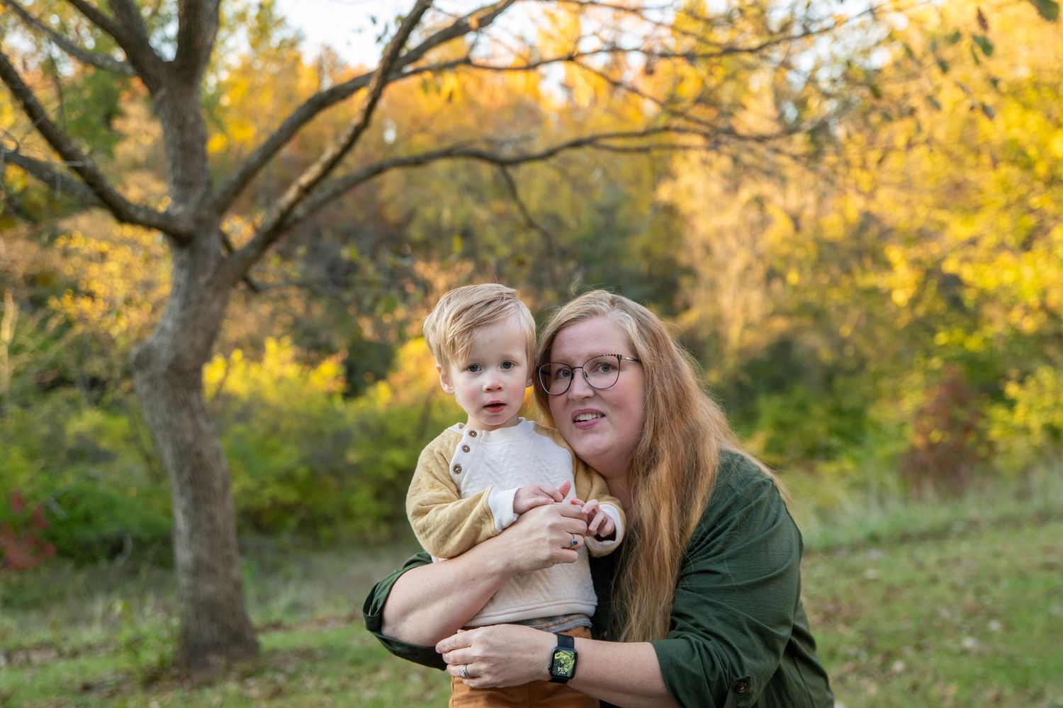 A tender family moment captured outdoors during golden hour with fall colors in the background.