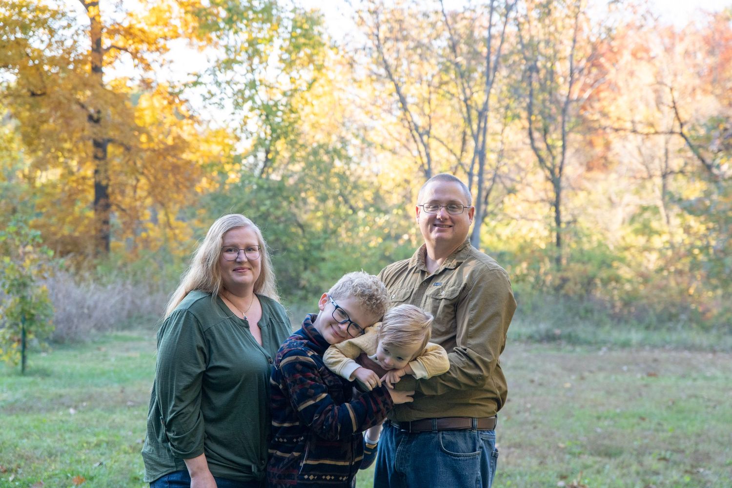 People share joyful moments together in an autumn field with trees displaying fall colors.
