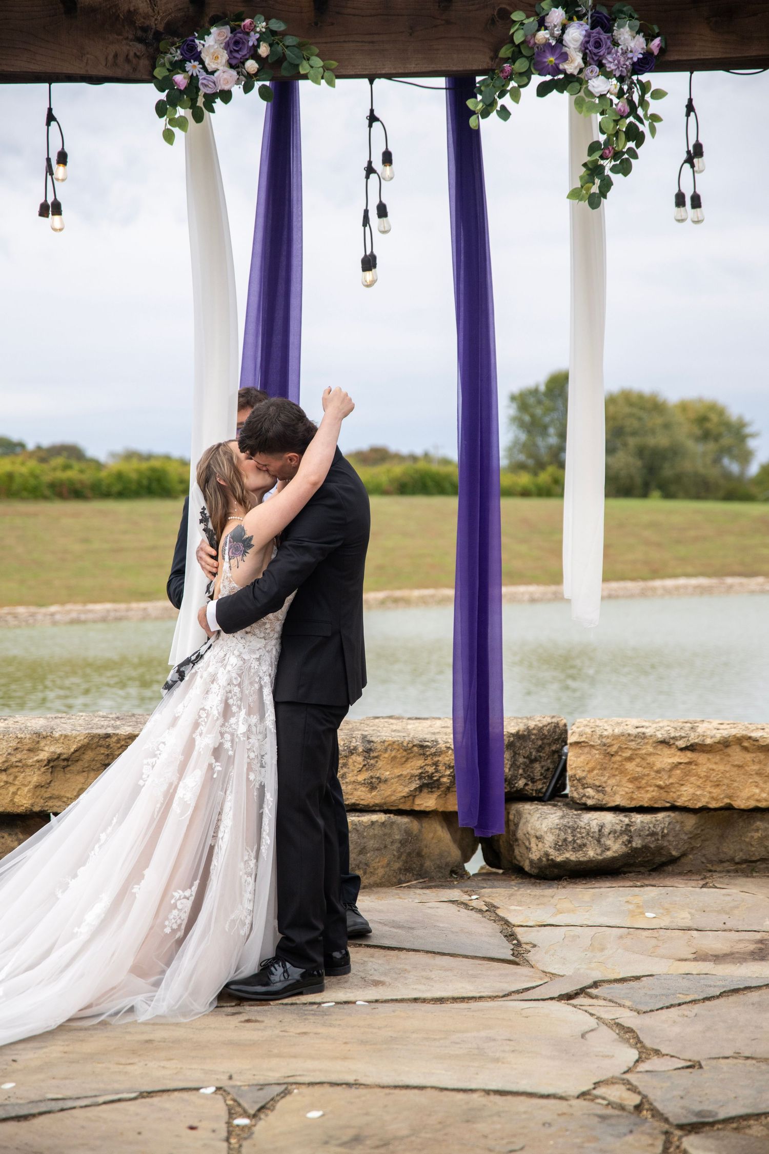 Couple embracing during their first kiss at lakeside wedding ceremony.