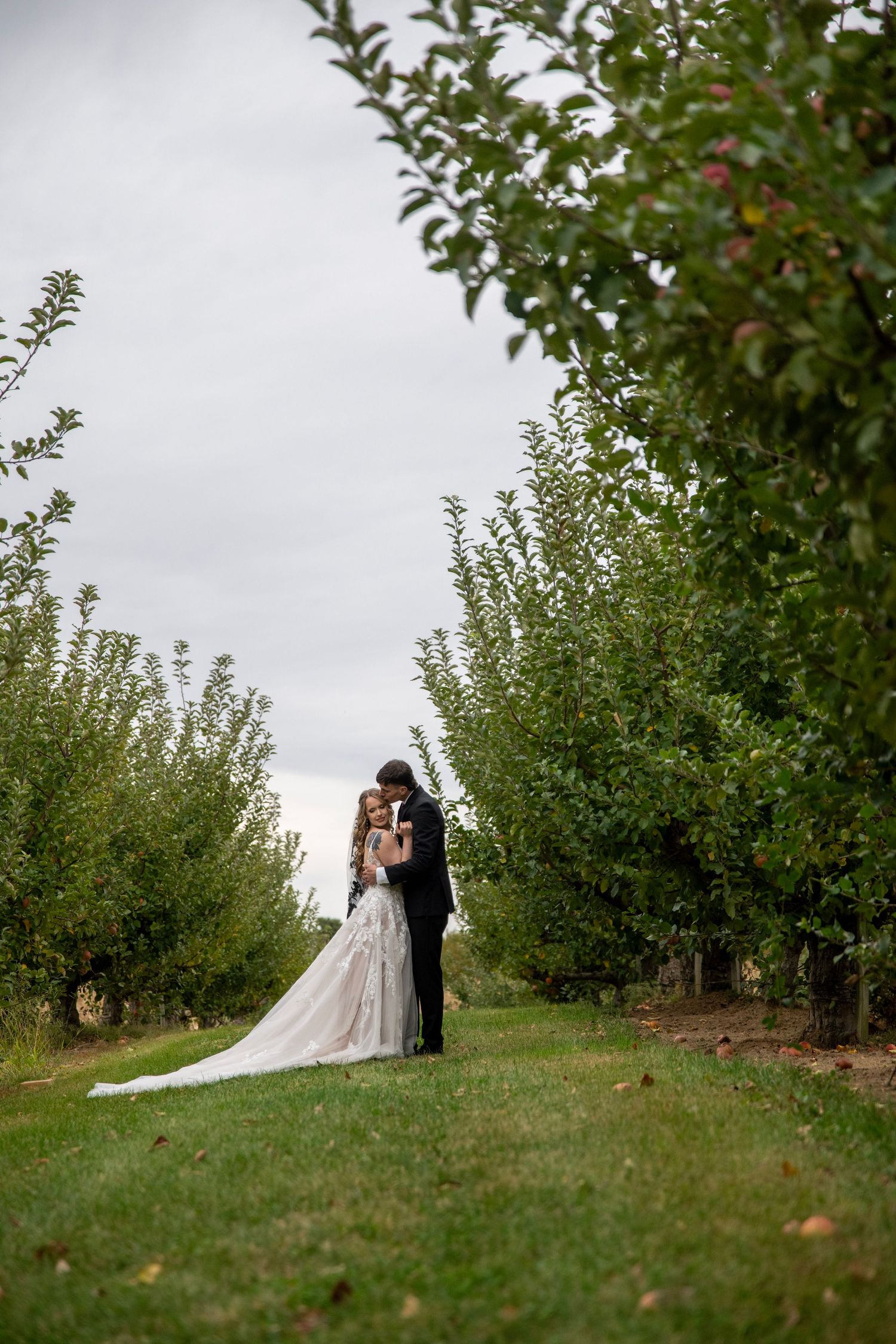 Romantic portrait of couple among orchard trees with flowing wedding dress train.