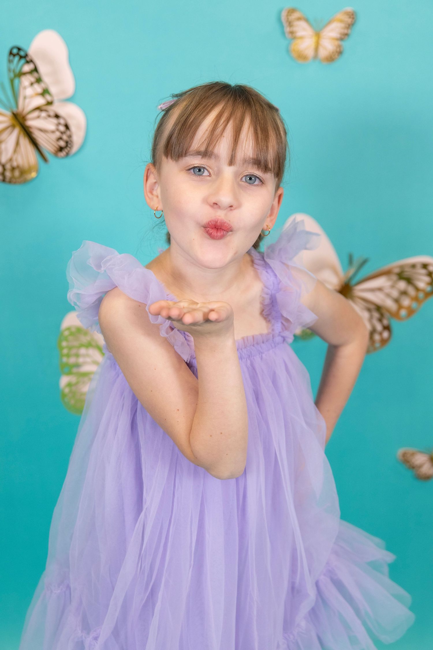 Whimsical portrait with butterfly decorations against turquoise background featuring purple tulle dress.