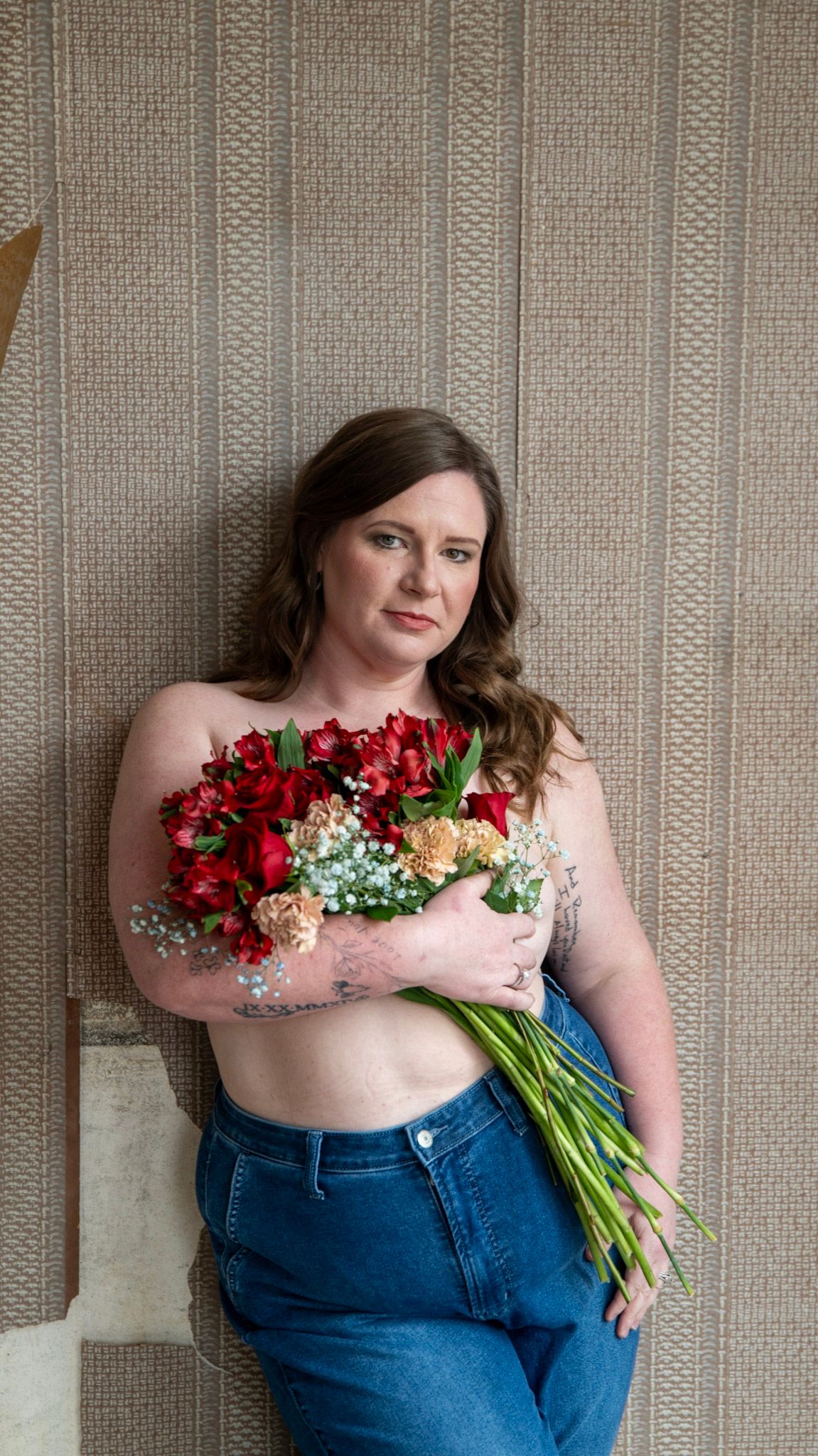 Artistic pose against distressed wall holding colorful bouquet with roses and baby's breath.