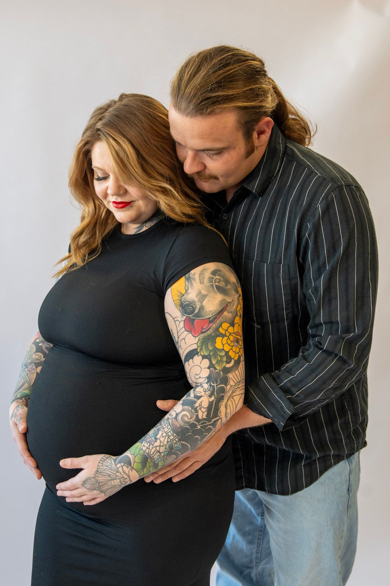 Couple embracing and cradling baby bump in pinstripe suit and black dress.