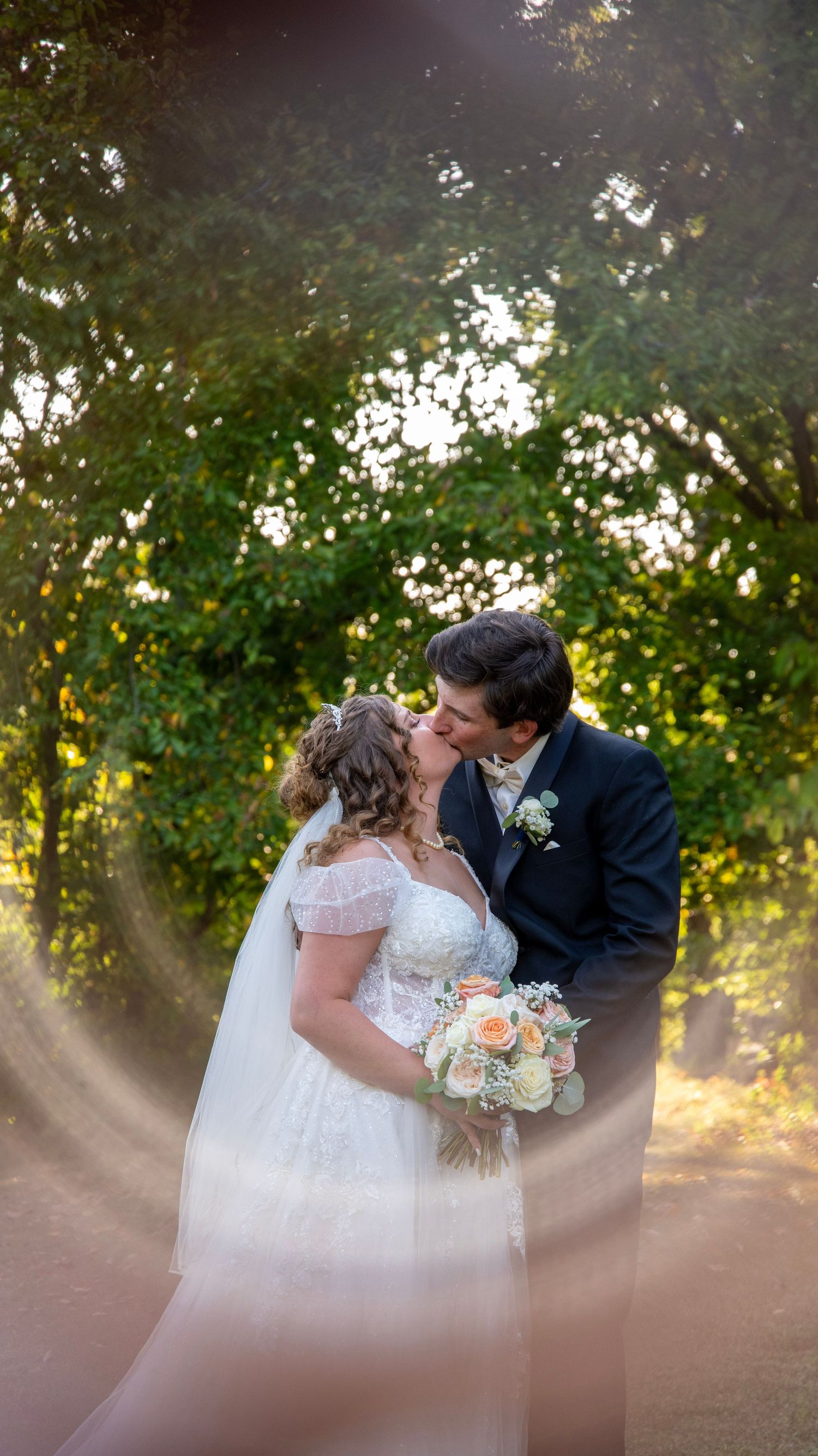 Romantic sunset wedding portrait through trees with soft golden lighting.