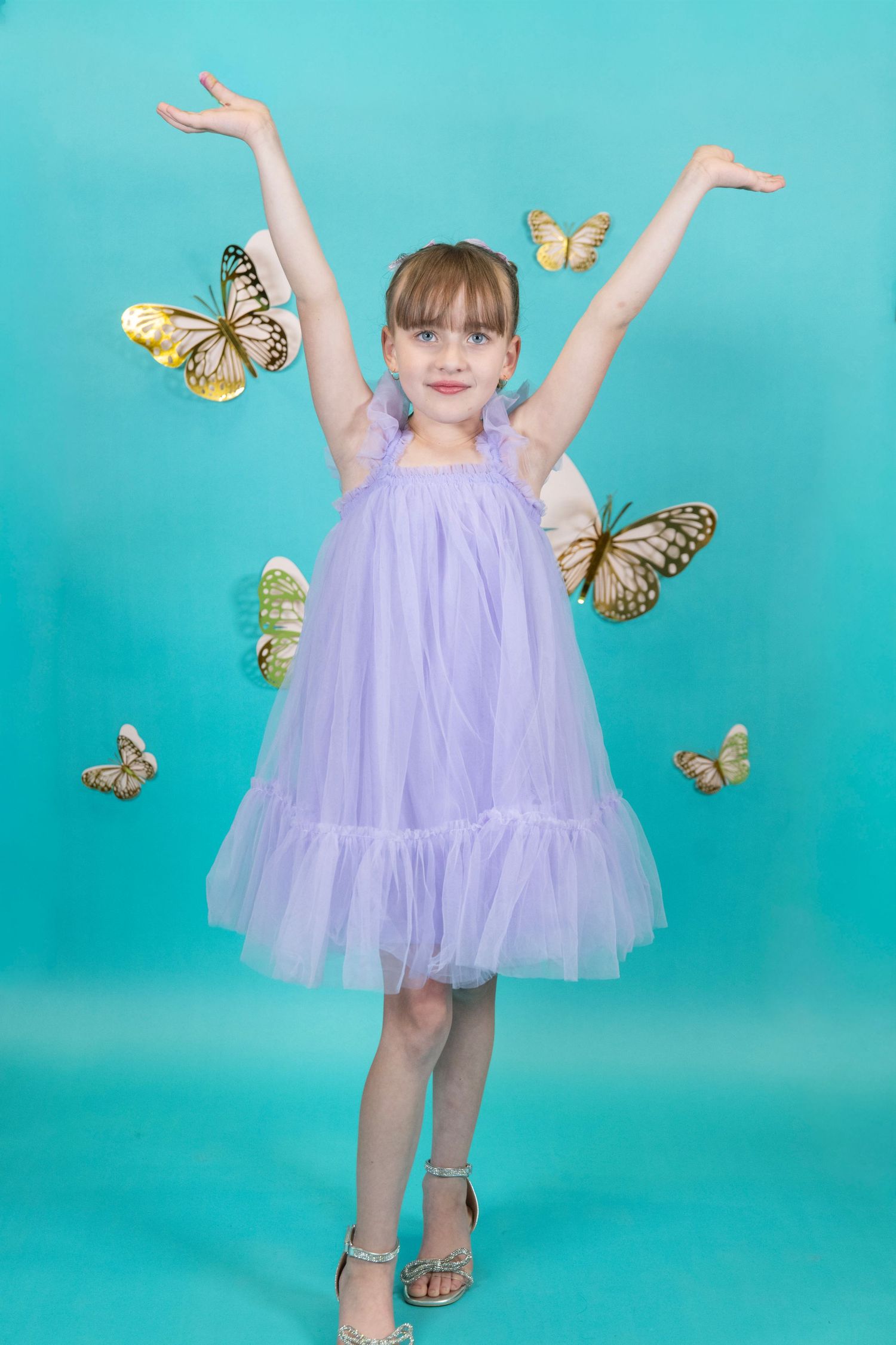 Arms raised joyfully in a purple tulle dress with floating butterflies on turquoise.