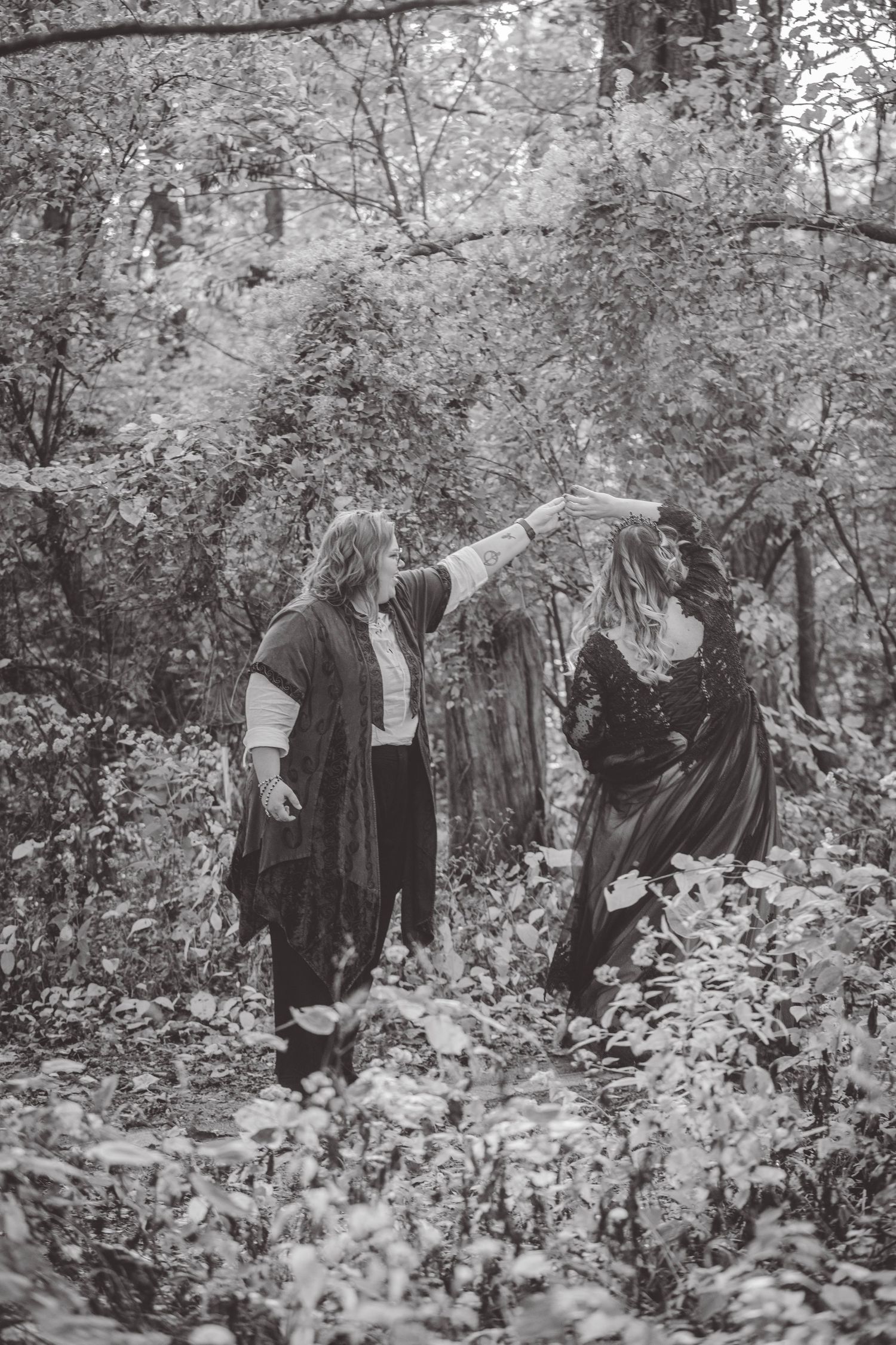 Black and white photo of people in Victorian-style clothing walking through a wooded area.